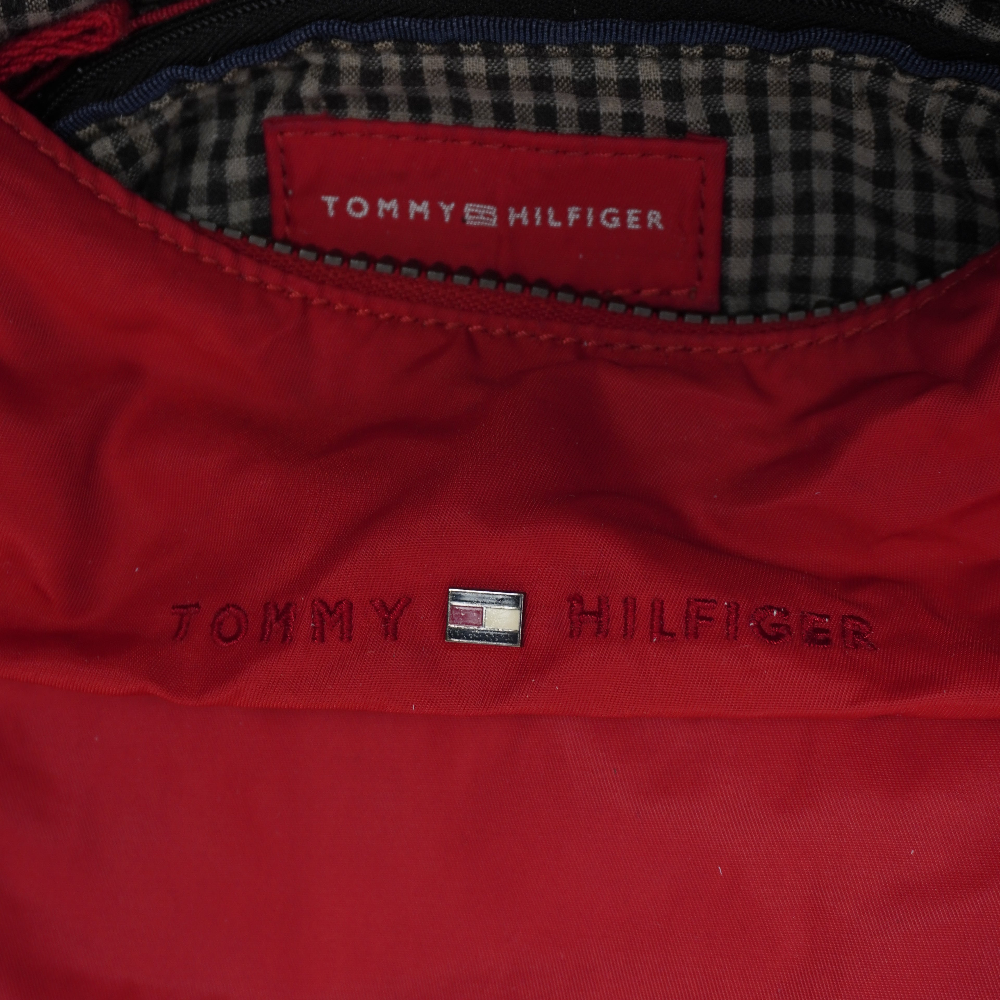 Primo piano della targhetta rettangolare in pelle rossa interna con scritta argento del brand e logo esterno ricamato tono su tono.