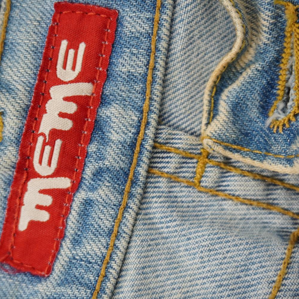 Primo piano dell'etichetta rettangolare rossa originale con logo bianco MEME cucita sulla cintura posteriore del jeans.