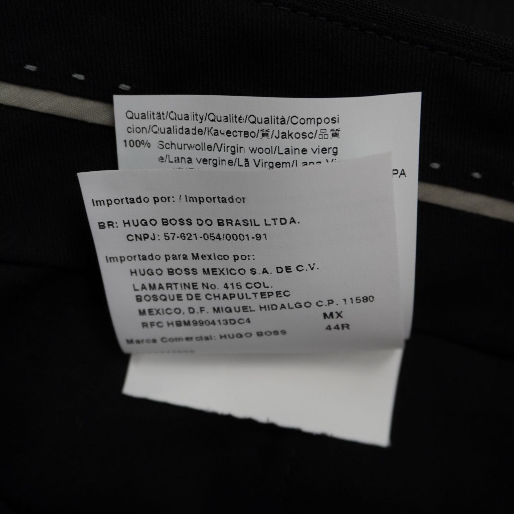 Macro dell'etichetta tecnica in tessuto bianco recante l'indicazione della taglia italiana 54 e la composizione in lana vergine.