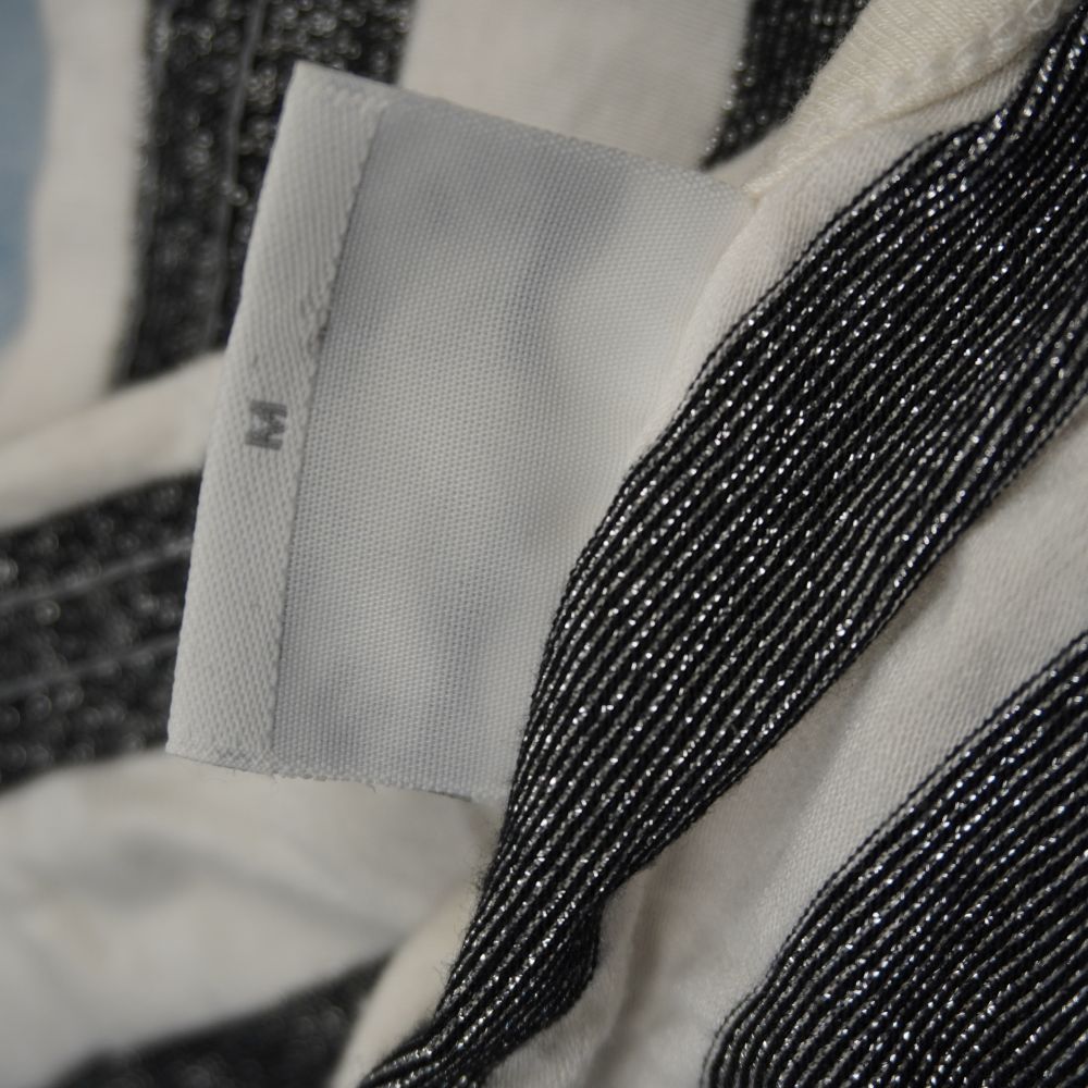  Ingrandimento dell'etichetta interna che mostra la taglia M (Medium) cucita sul bordo del top a righe con evidente trama brillante in lurex argento.