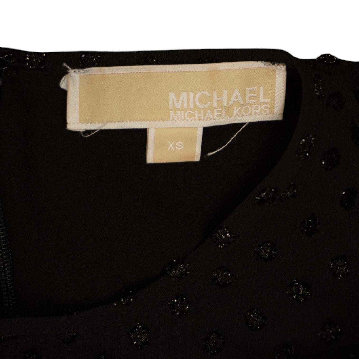 Dettaglio della classica targhetta metallica dorata rettangolare con il logo Michael Kors cucita all'interno dello scollo.
