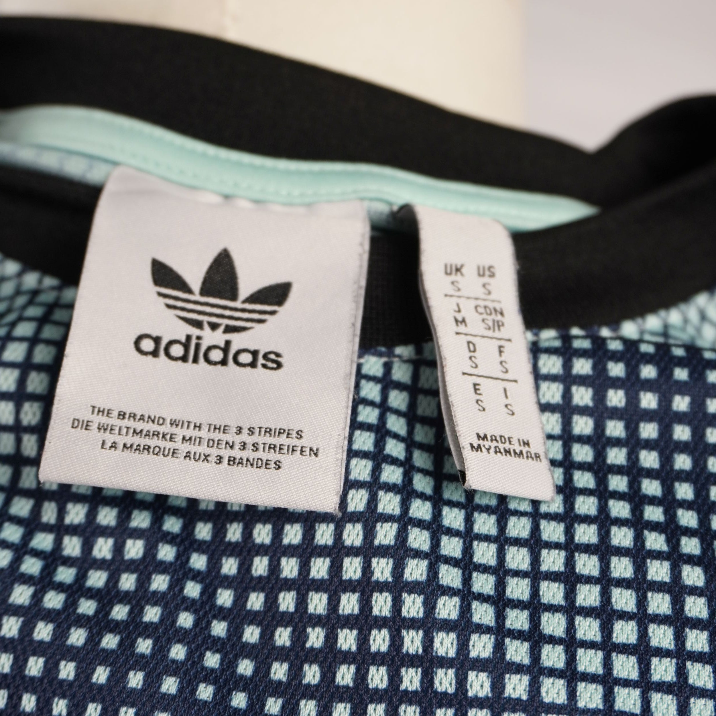 Etichette sul colletto con logo adidas Originals e griglia delle taglie internazionali che indica la taglia italiana S.