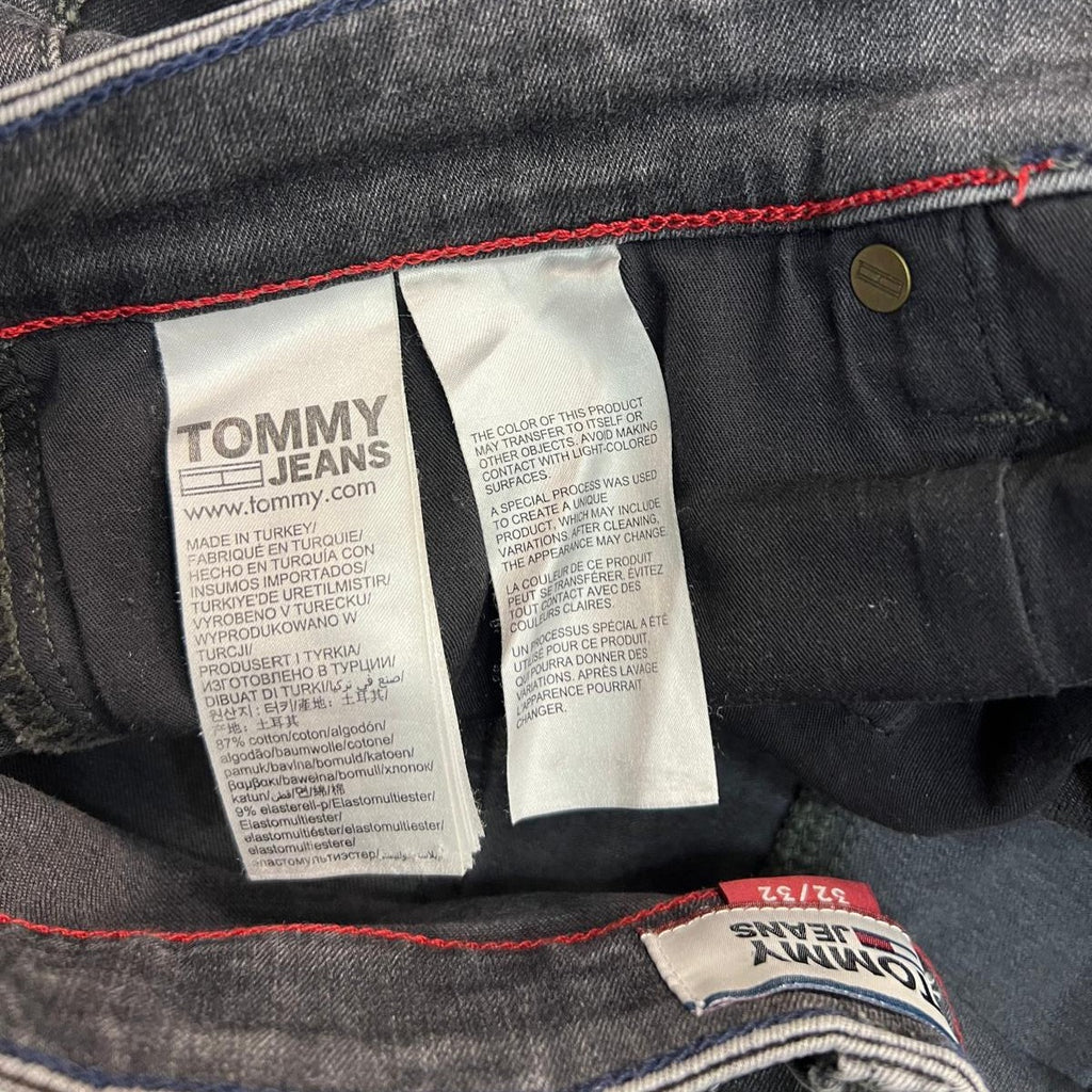  Inquadratura ravvicinata del gruppo di etichette interne in tessuto bianco fissate alla cucitura della vita dei jeans grigi.