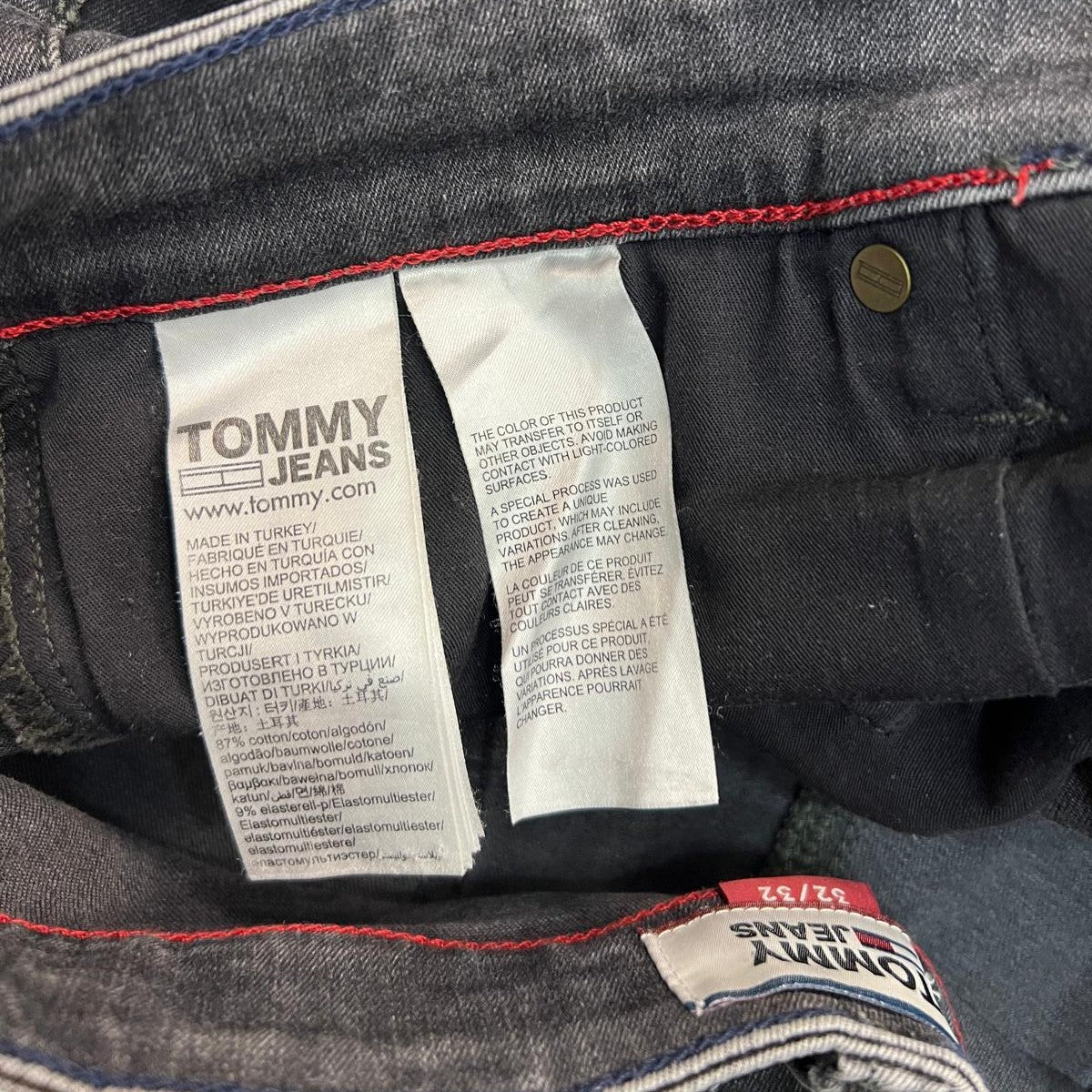  Inquadratura ravvicinata del gruppo di etichette interne in tessuto bianco fissate alla cucitura della vita dei jeans grigi.