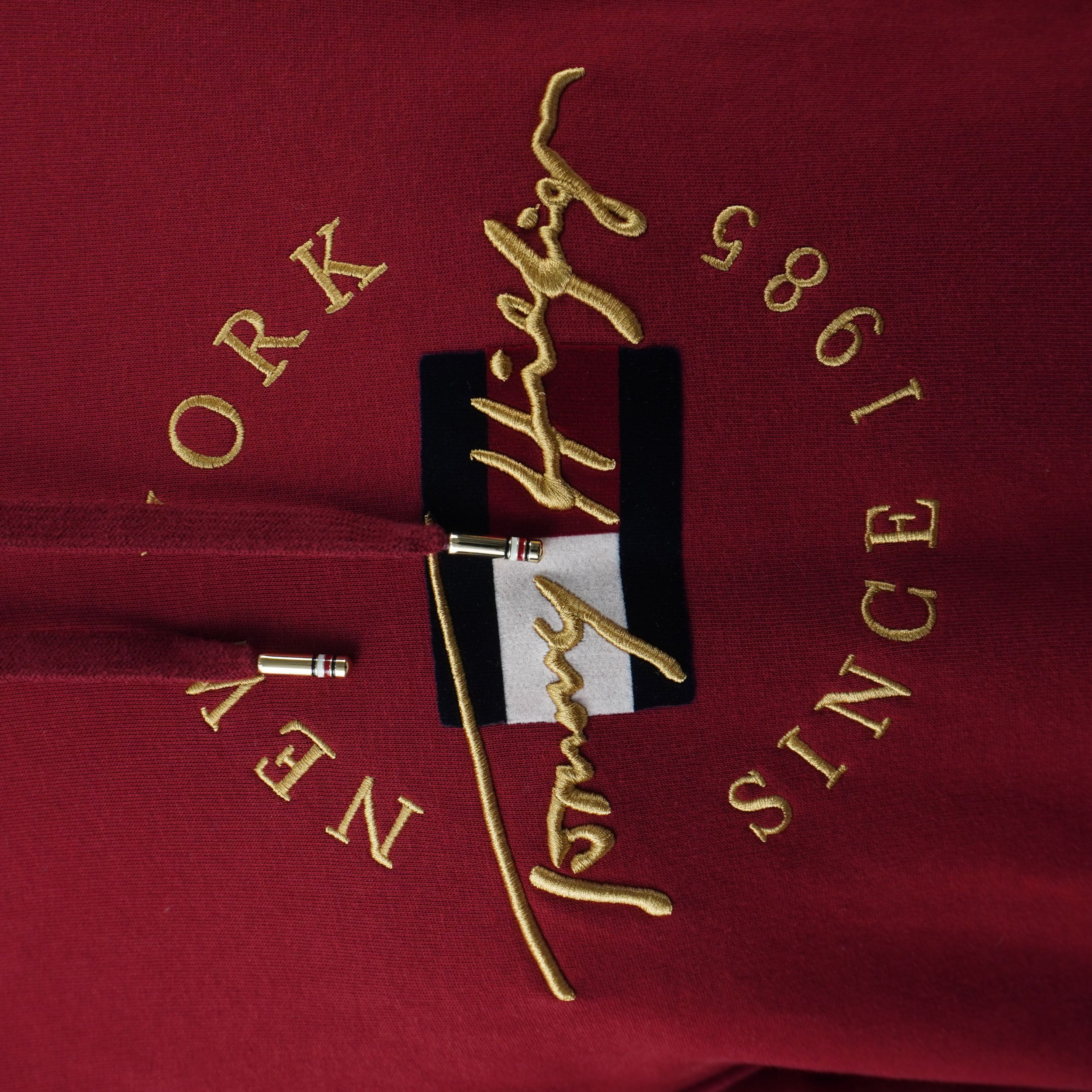 Primo piano del ricamo dorato frontale "Tommy Hilfiger New York Since 1985" sul petto.