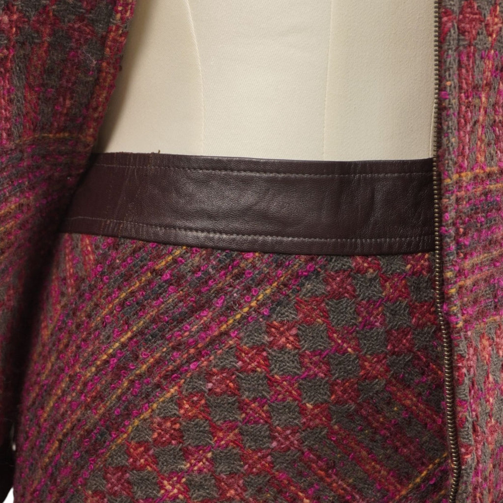 Dettaglio ravvicinato della trama tweed bordeaux e del profilo inferiore della giacca in pelle nera.