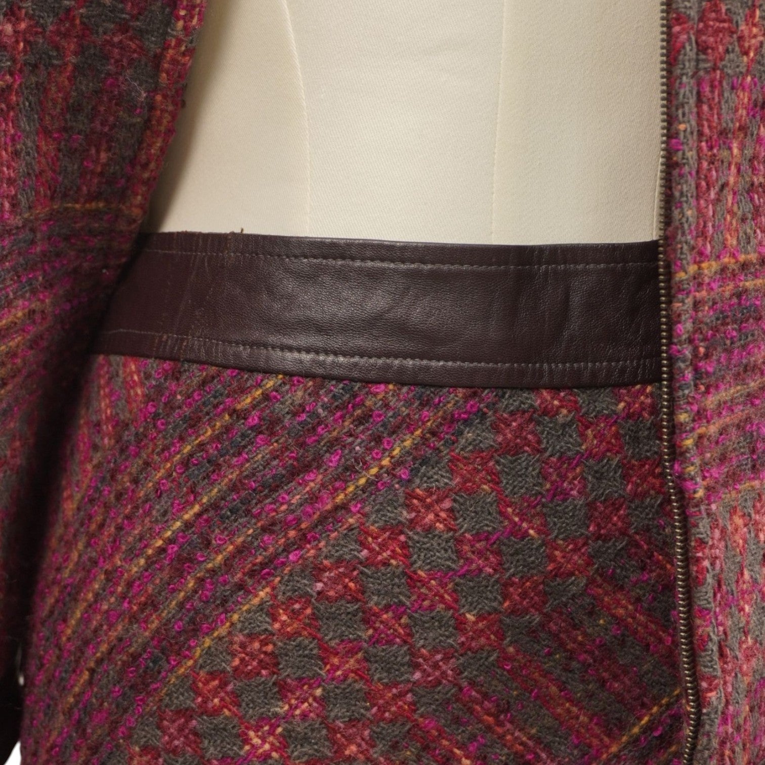 Dettaglio ravvicinato della trama tweed bordeaux e del profilo inferiore della giacca in pelle nera.