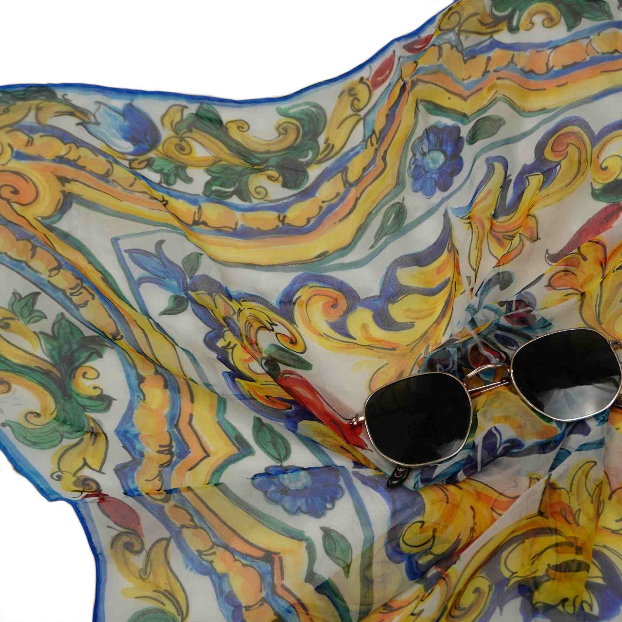 Dettaglio della stampa Maiolica del foulard Dolce & Gabbana accostato a un paio di occhiali da sole neri, look estivo luxury.