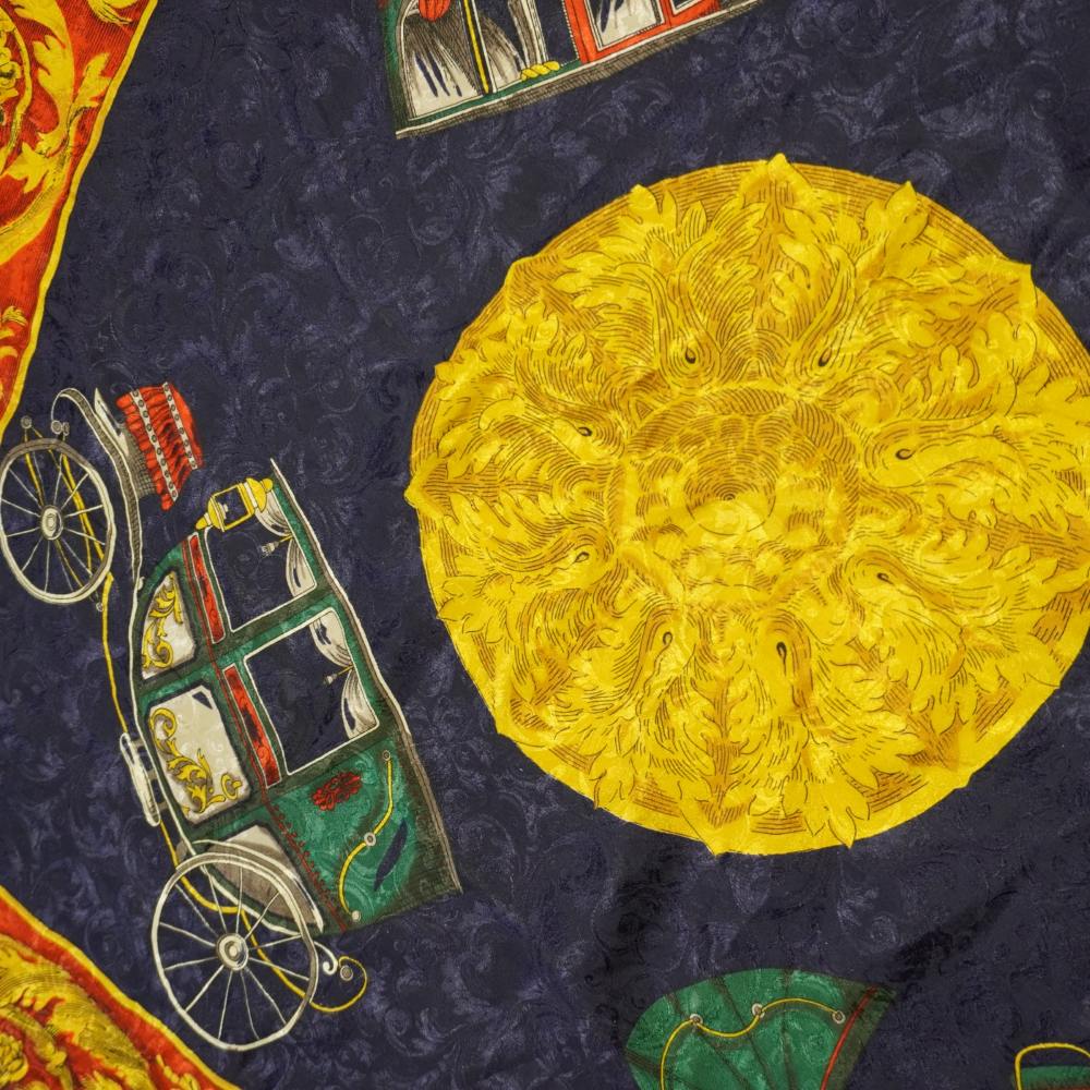 Ingrandimento del motivo centrale con grande sole giallo oro e illustrazione di una carrozza d'epoca verde e rossa su sfondo in seta jacquard damascata blu notte.