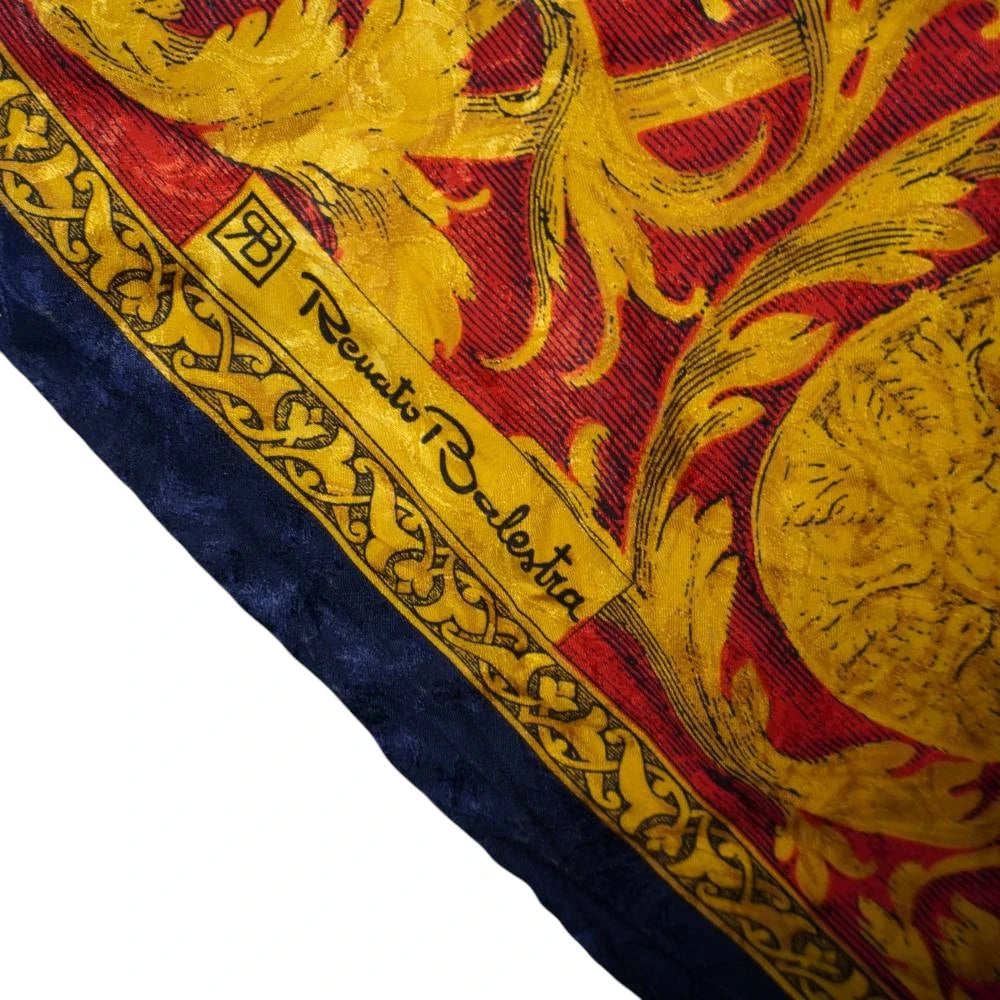 Ingrandimento ravvicinato dell'angolo del foulard che mostra il monogramma geometrico con le lettere RB e la firma ufficiale stampata Renato Balestra su cornice barocca.