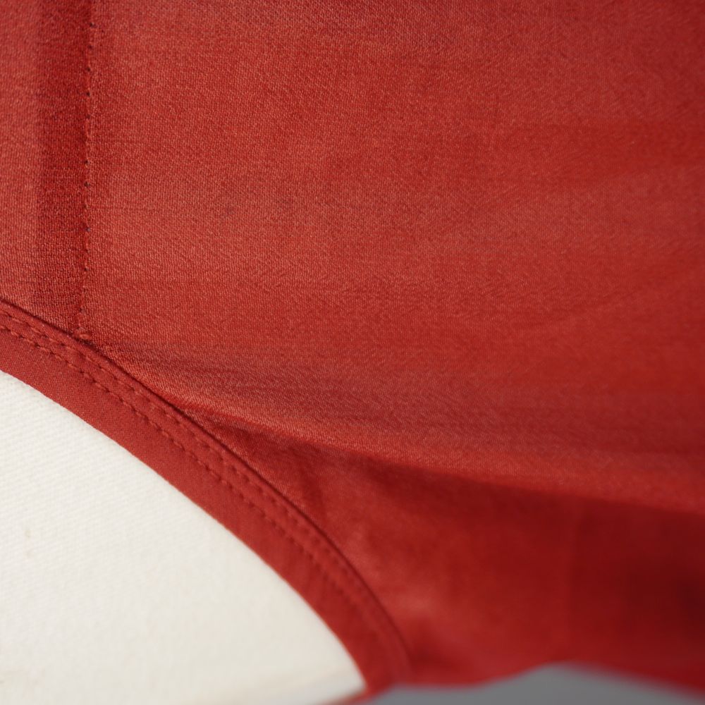  Ingrandimento ravvicinato sulla trama del tessuto liscio rosso ruggine e sulla linea di cucitura vicino al giromanica del top.