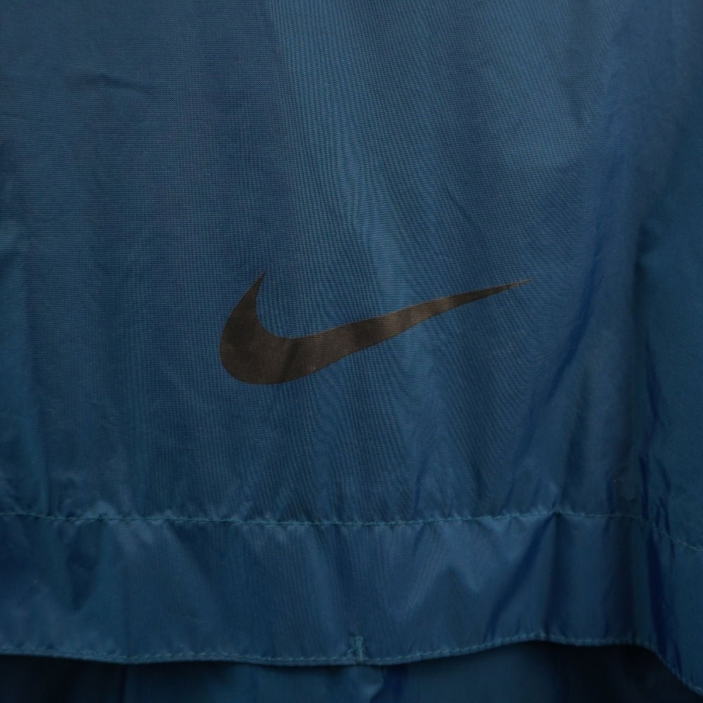 Primo piano del logo Nike Swoosh ricamato in filo rosso a contrasto sul petto del tessuto in nylon blu.