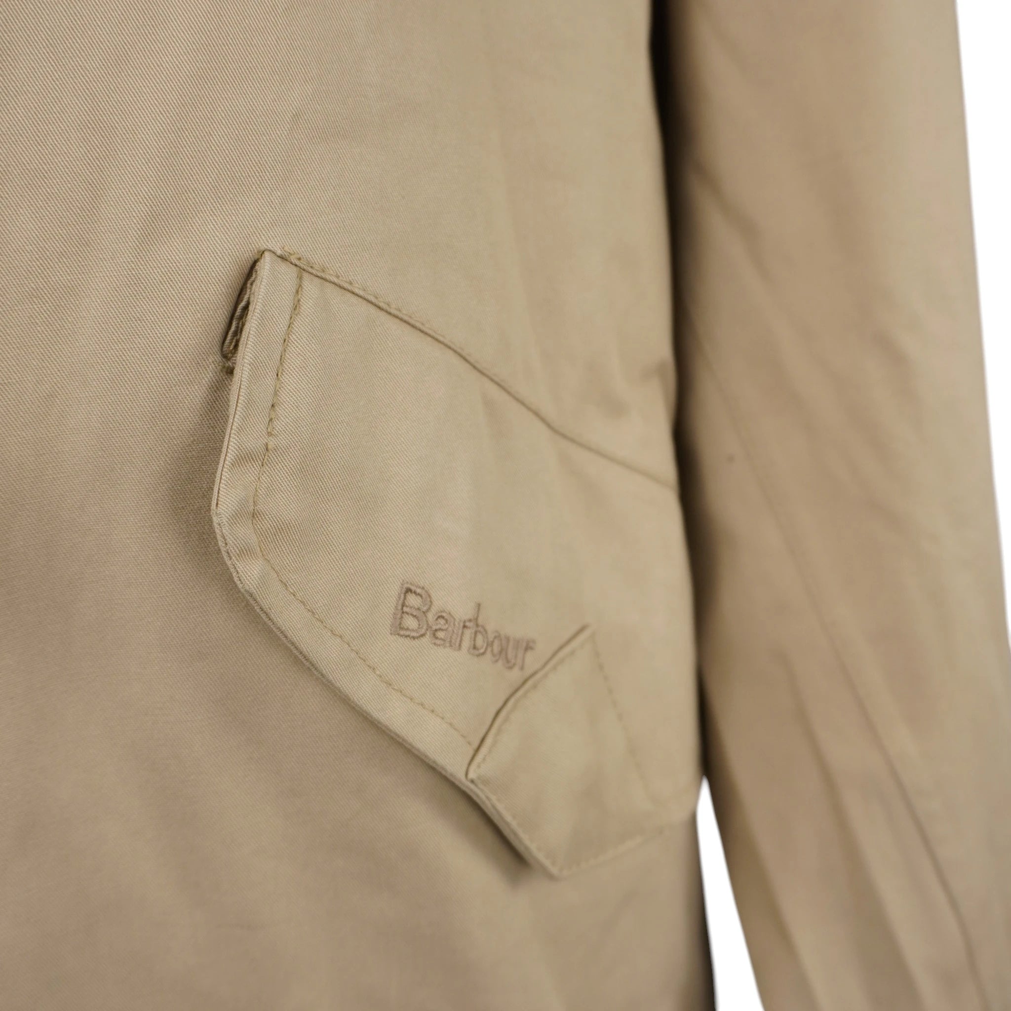  Inquadratura ravvicinata della tasca frontale sbieca a pattina della giacca Barbour con logo del brand ricamato tono su tono.