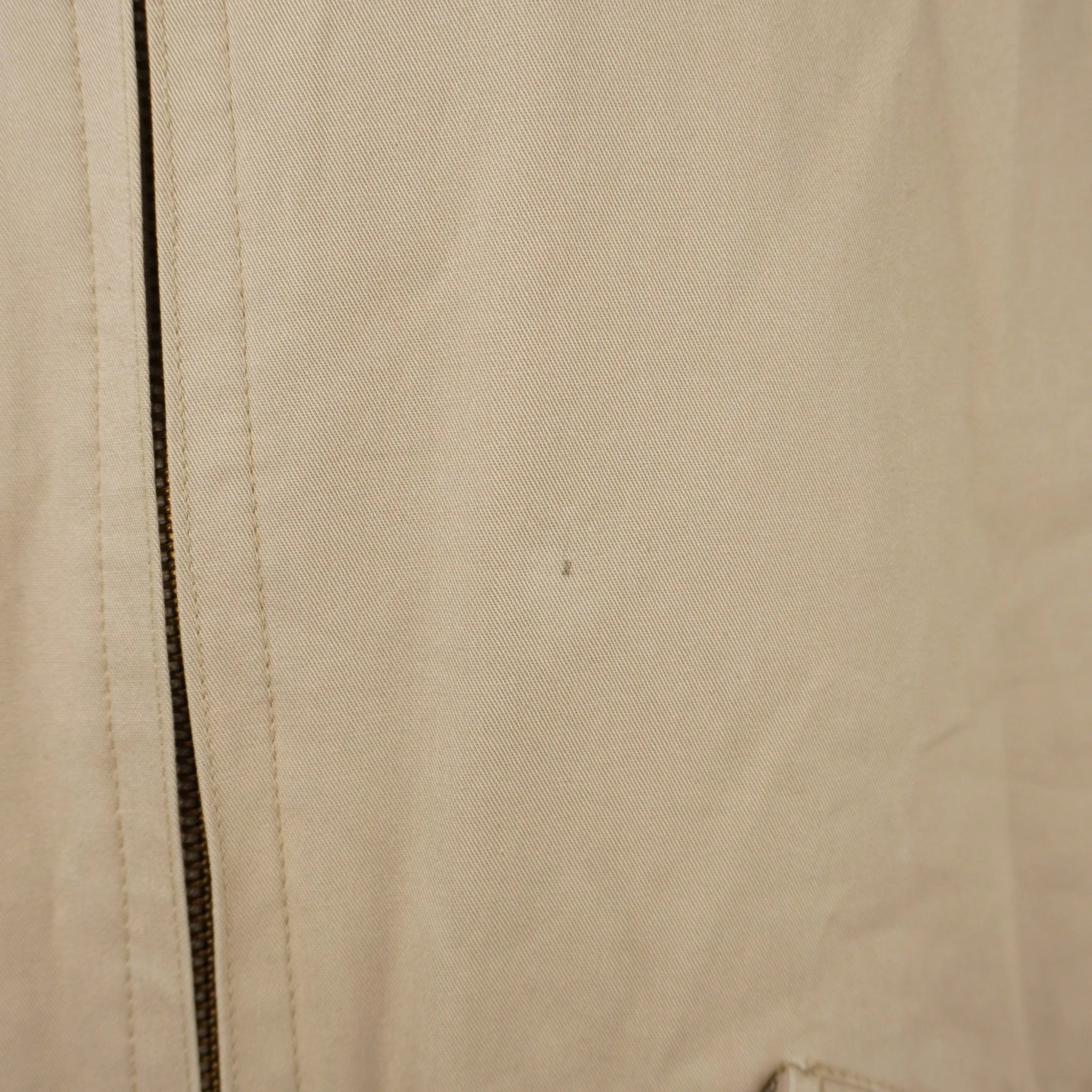 Dettaglio del tessuto in cotone beige della giacca Barbour che mostra una piccola macchia scura millimetrica vicino alla zip.