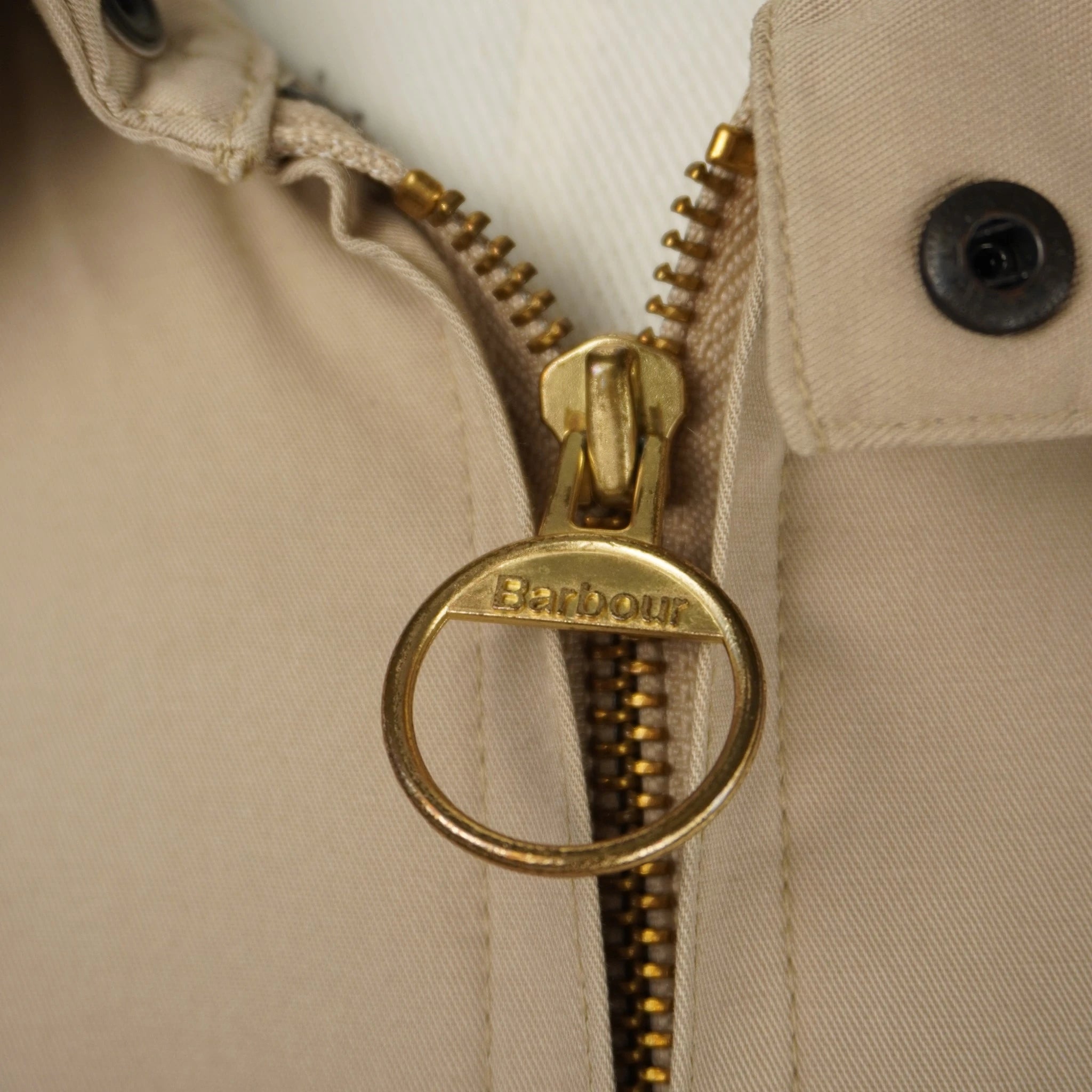Primo piano della cerniera lampo in ottone dorato della giacca Barbour con l'iconico cursore ad anello logato.