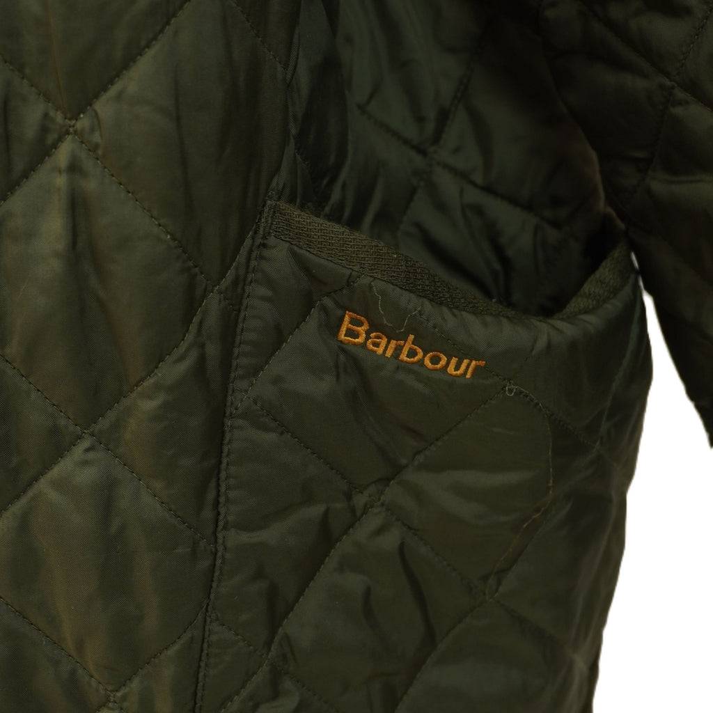  Primo piano della tasca applicata anteriore della giacca Barbour con focus sul logo del brand ricamato in filo marrone.