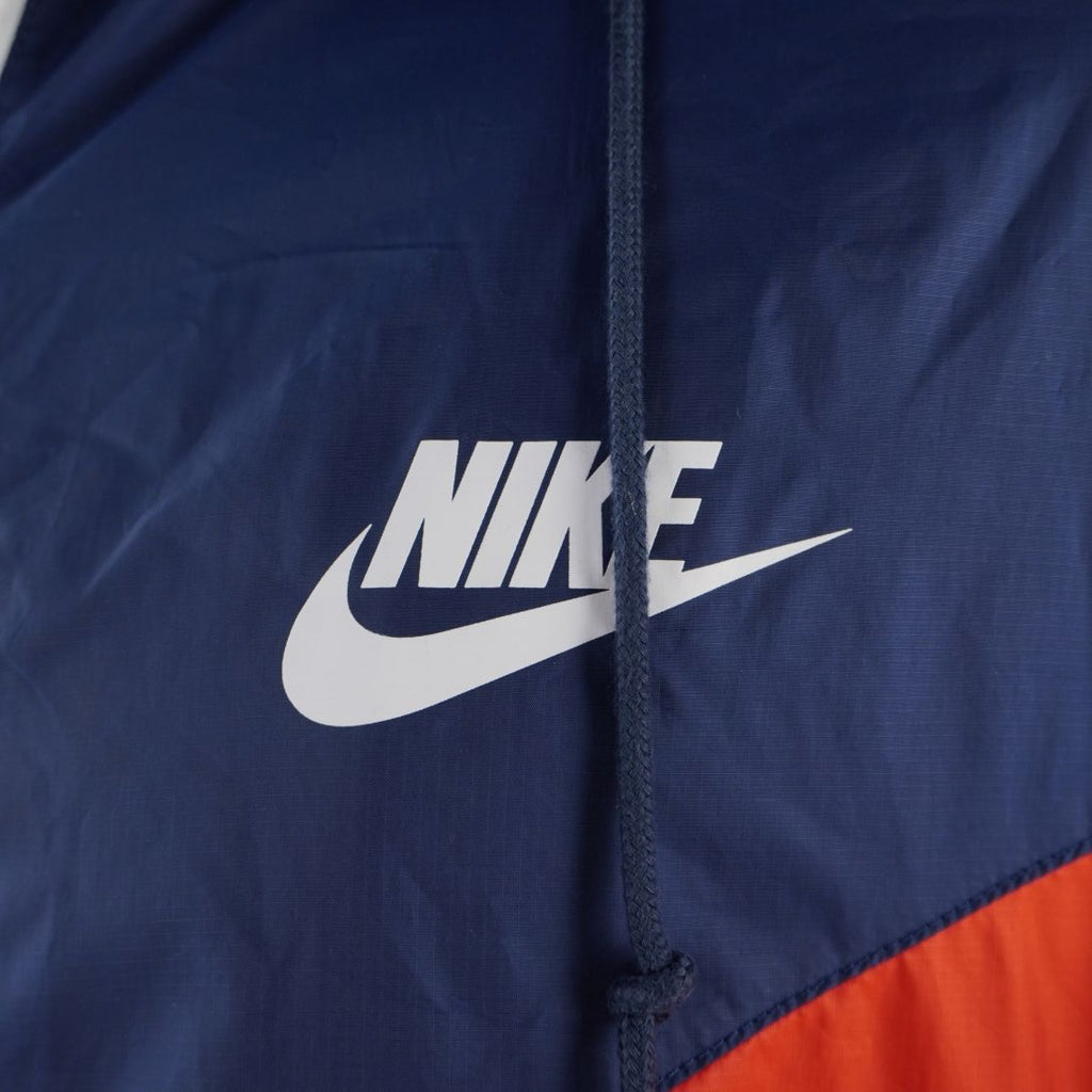 Dettaglio ravvicinato del classico logo Nike Futura bianco stampato sul petto della giacca a vento in tessuto blu navy.