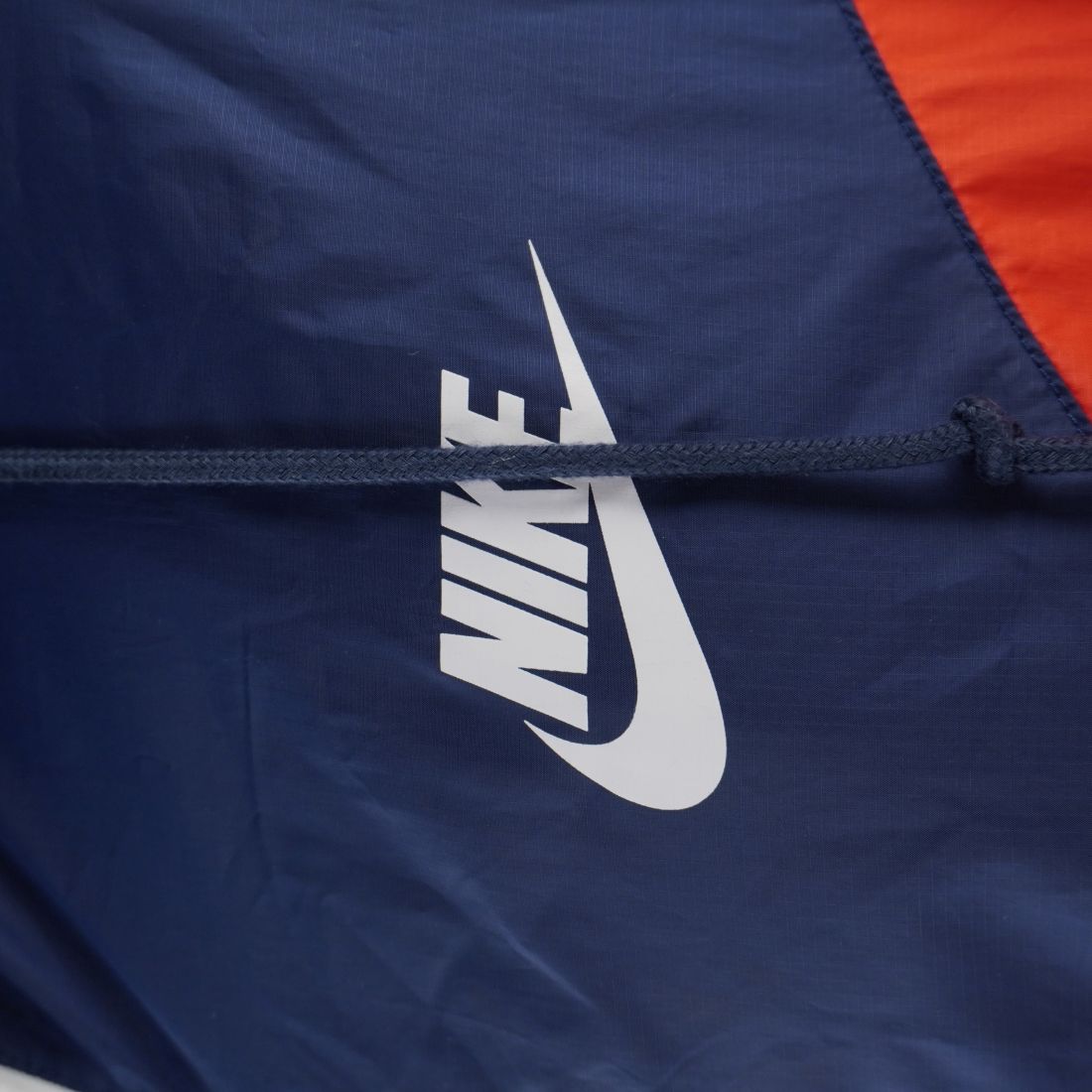 Dettaglio ravvicinato del classico logo Nike Futura bianco stampato sul petto della giacca a vento in tessuto blu navy.