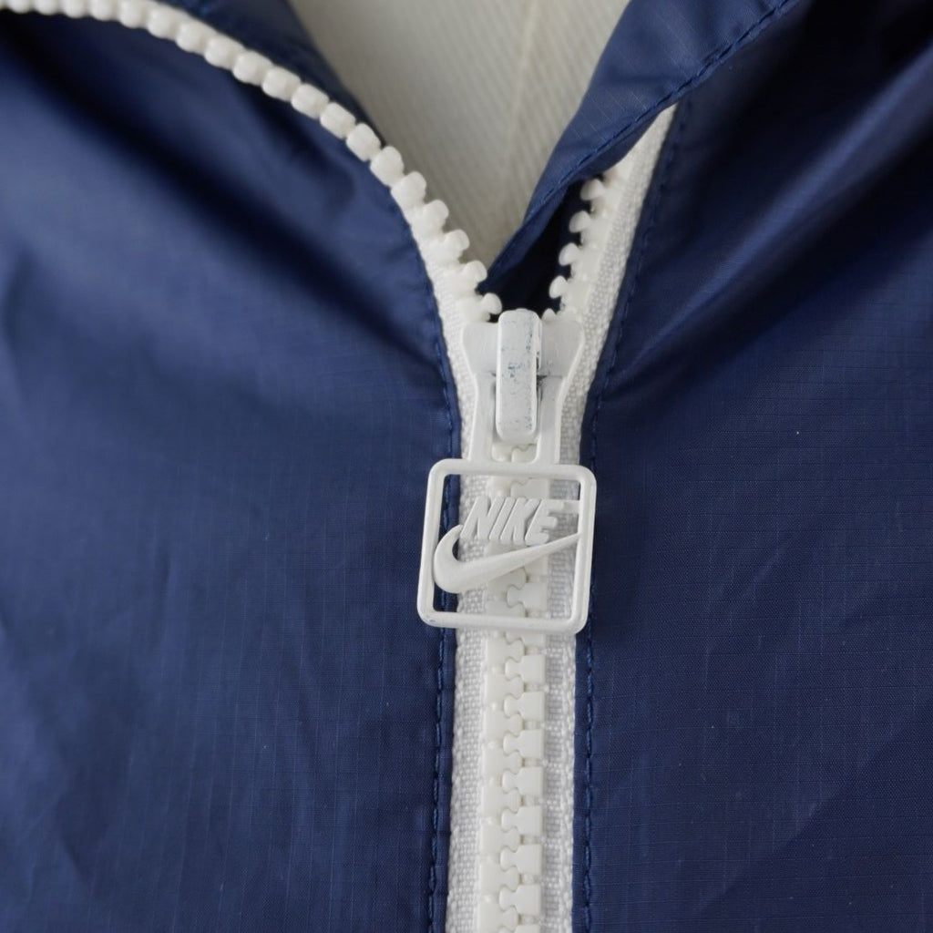 Zoom sulla chiusura centrale full-zip bianca con cursore in metallo logato Nike Futura su sfondo in tessuto blu.