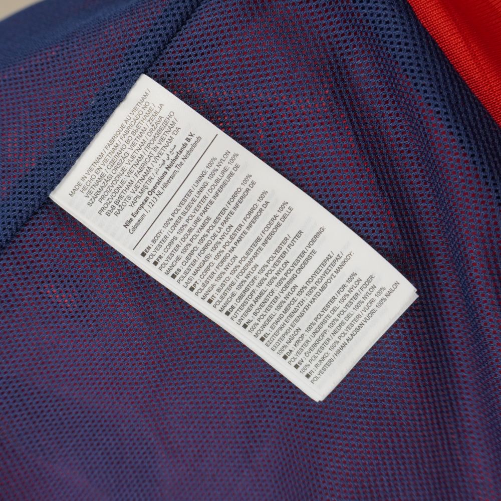 Dettaglio dell'etichetta interna multi-foglio con le specifiche di composizione in poliestere e nylon in diverse lingue.