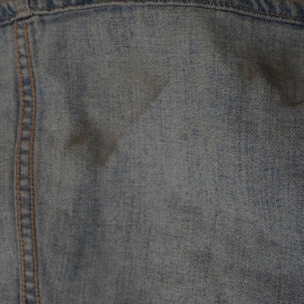 Inquadratura ravvicinata del tessuto denim chiaro del gilet Versace Jeans Couture che mostra una piccola macchia scura superficiale.