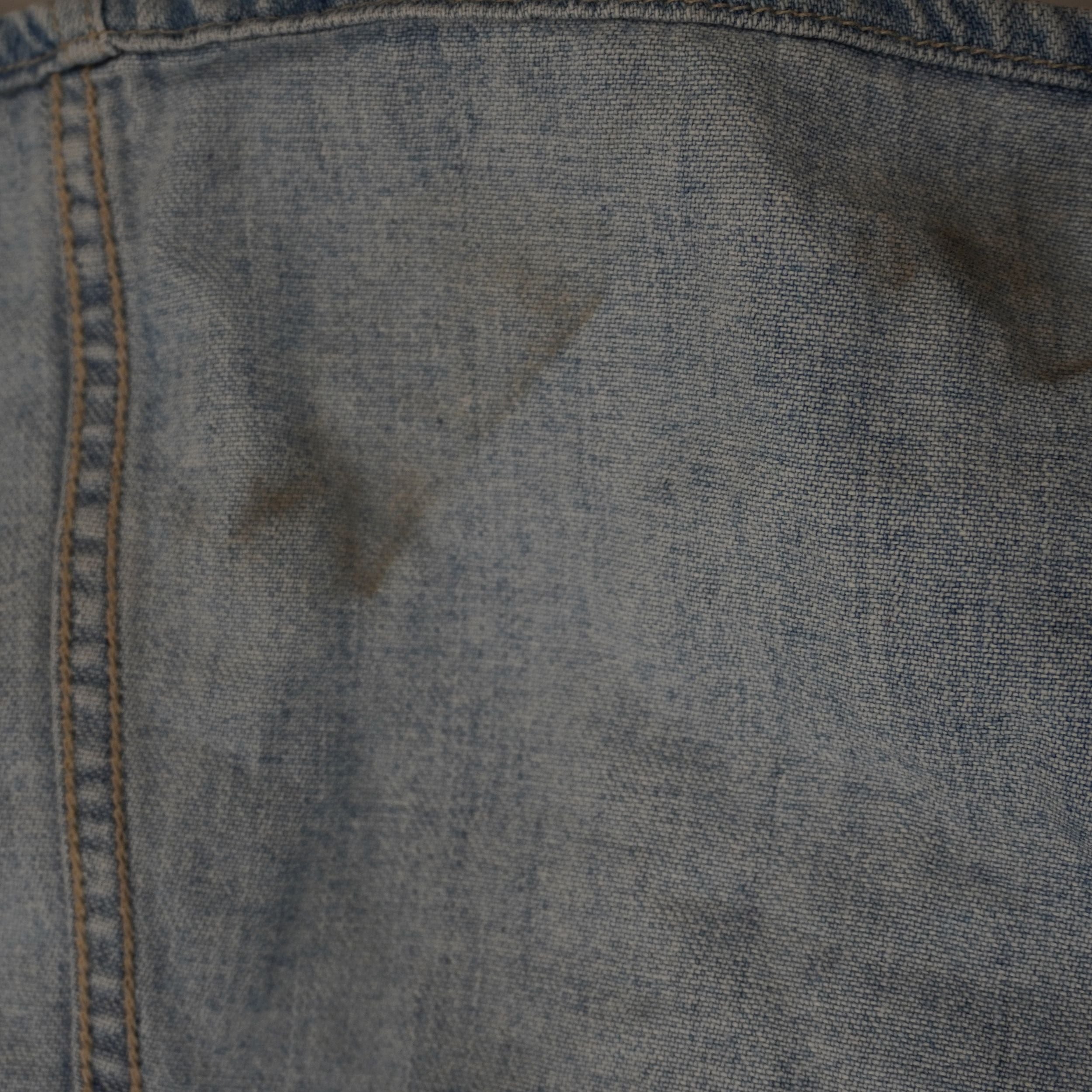 Inquadratura ravvicinata del tessuto denim chiaro del gilet Versace Jeans Couture che mostra una piccola macchia scura superficiale.