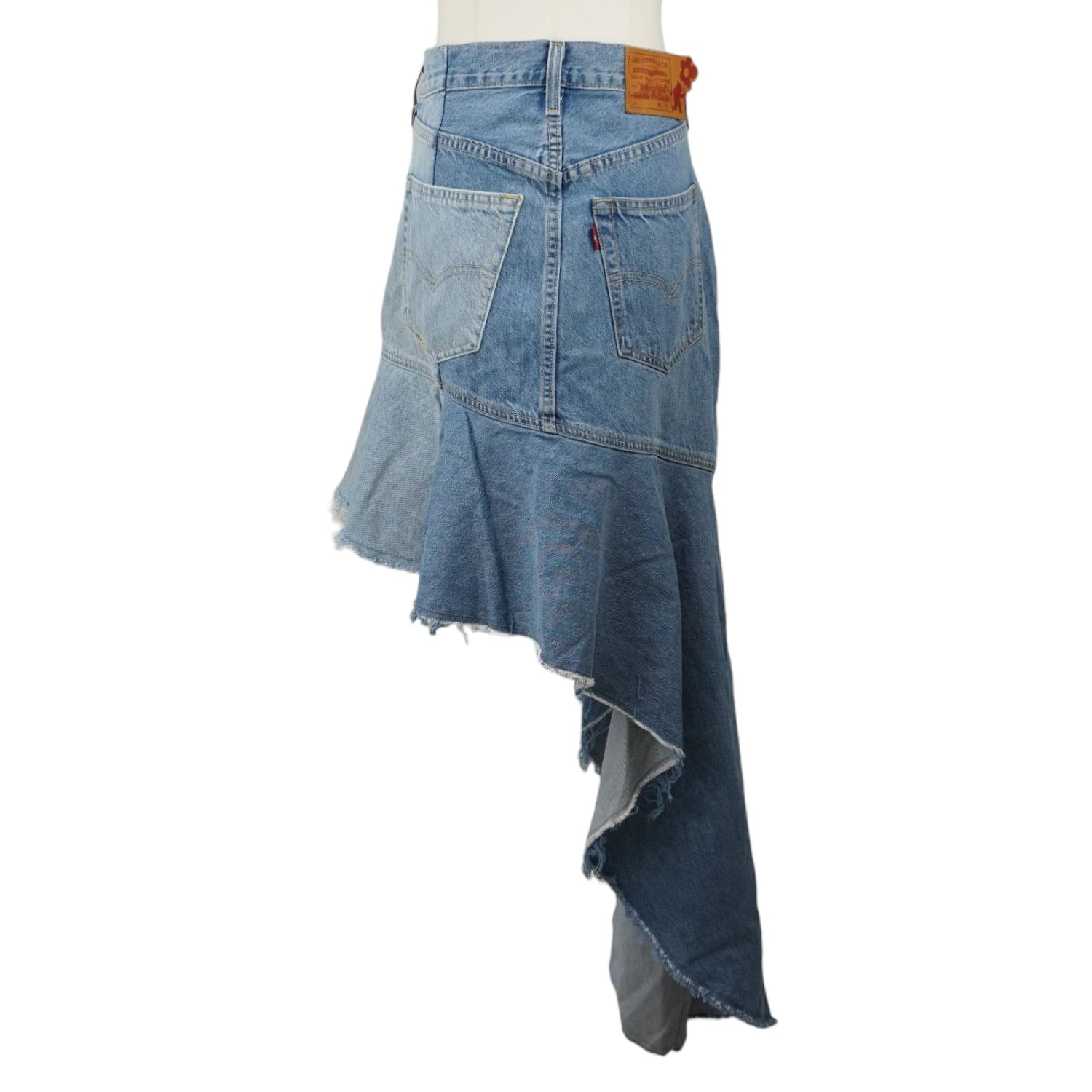 Profilo laterale della gonna di jeans che mostra lo sbalzo di lunghezze del maxi volant asimmetrico e l'orlo sfilacciato a taglio a vivo.