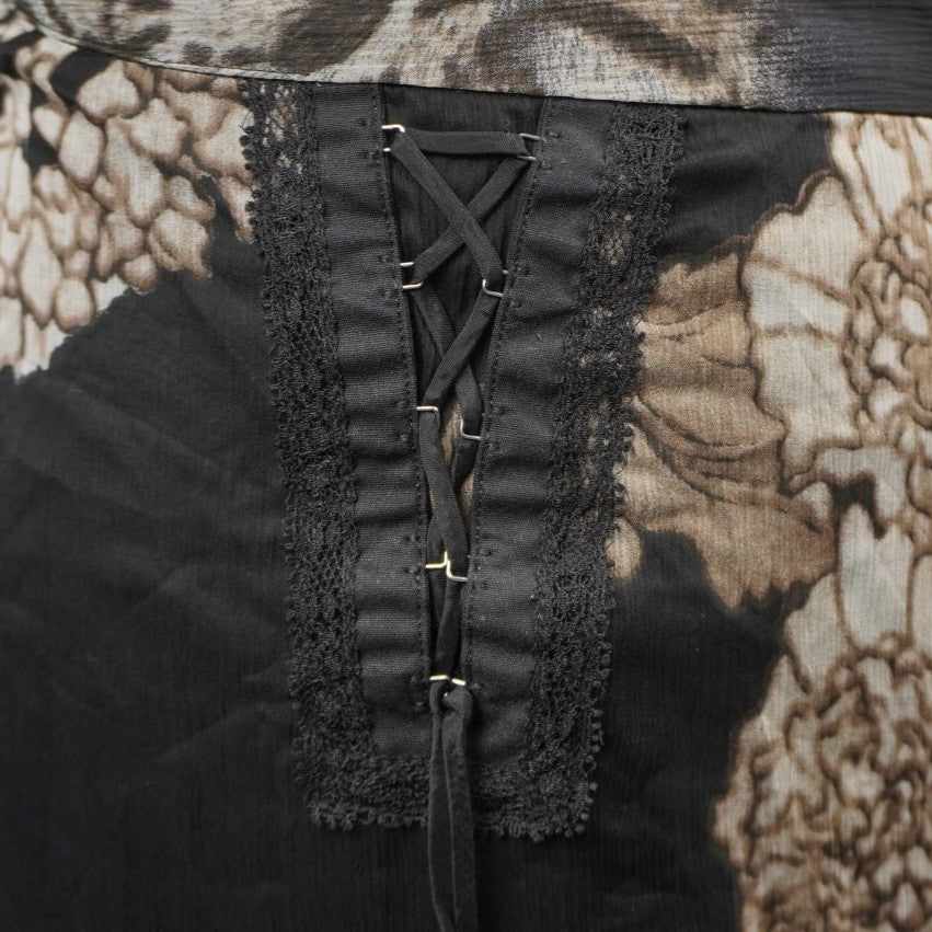 Primo piano del dettaglio laterale della gonna con allacciatura stringata stile corsetto regolabile tramite ganci metallici e bordo in pizzo nero ricamato.