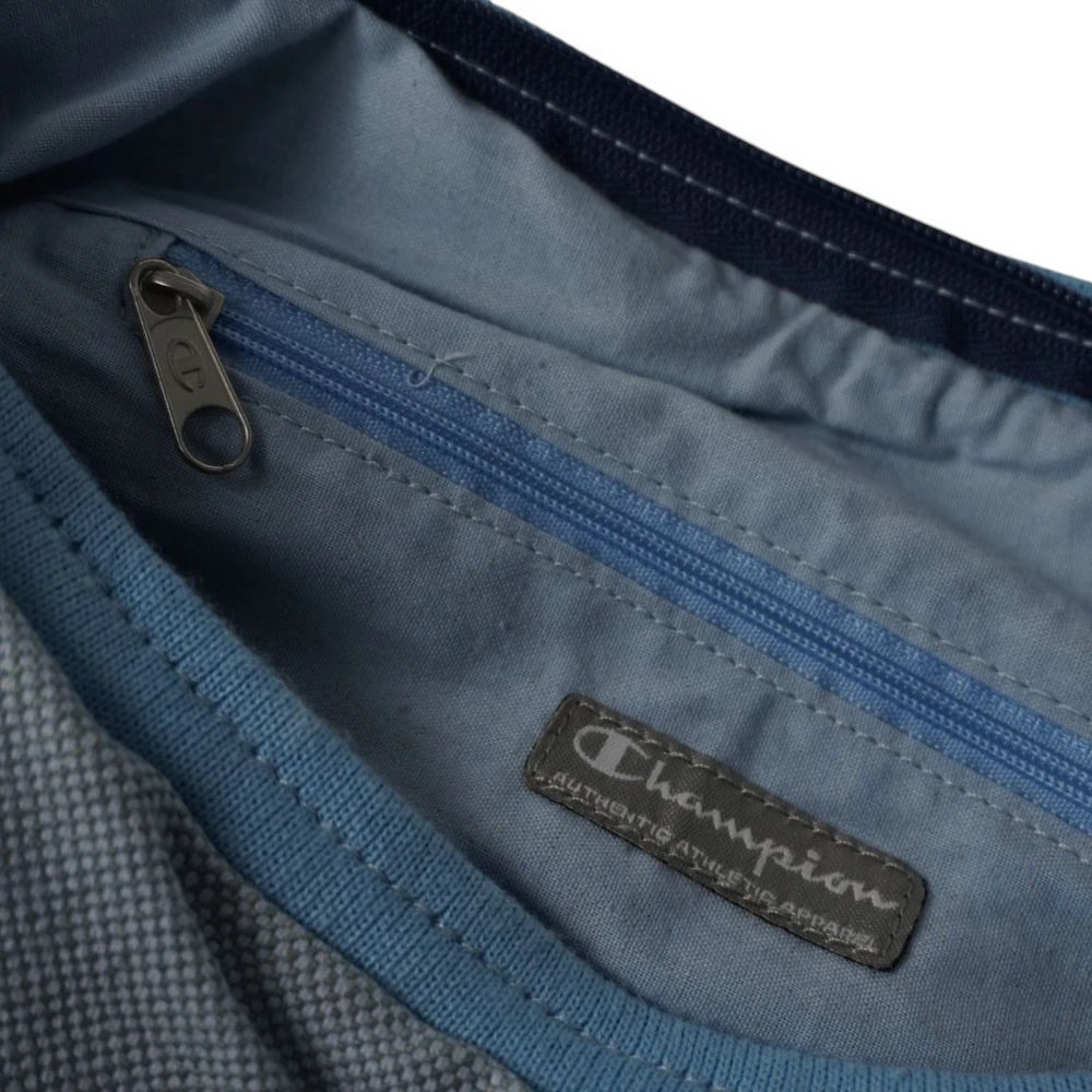 Vista dell'interno della borsa con fodera in tessuto azzurro, tasca di sicurezza dotata di zip ed etichetta cucita in similpelle marrone logata Champion.
