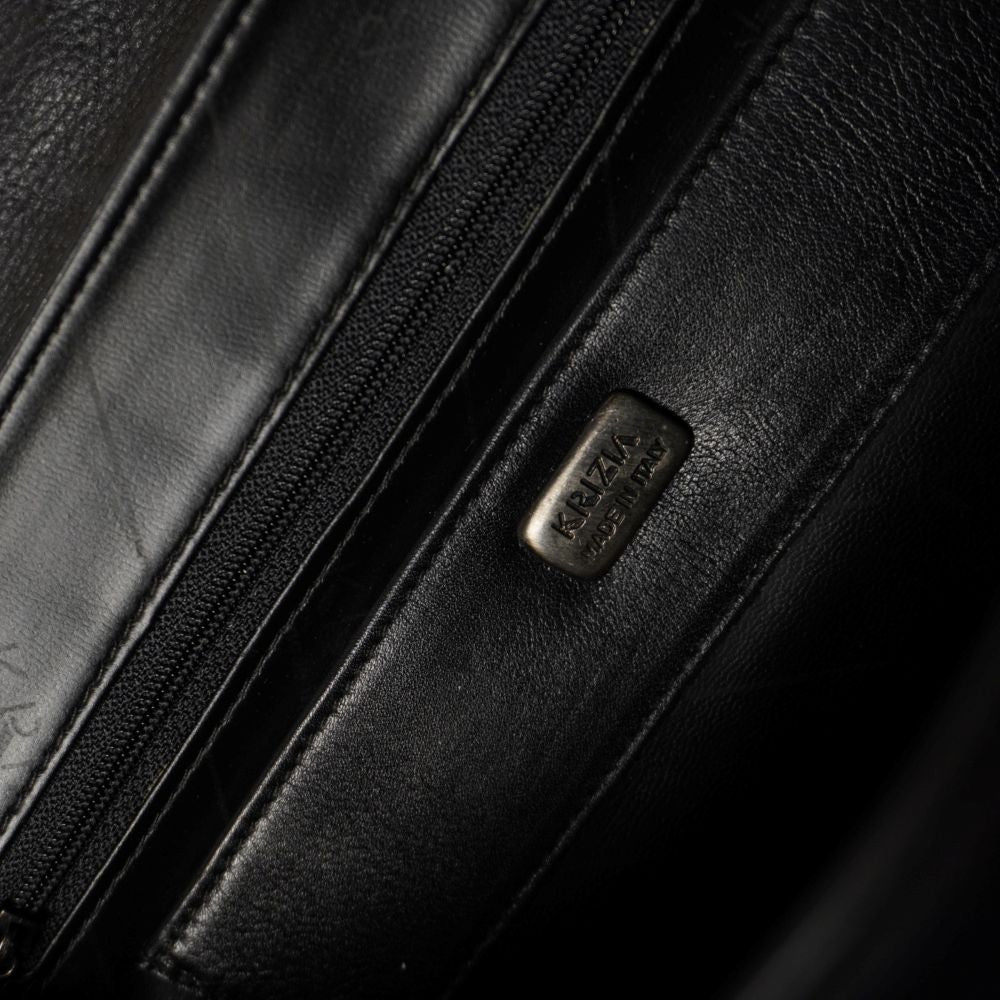 Vista interna della borsa che mostra la fodera scura, la tasca di sicurezza con cerniera lampo e la placchetta metallica lucida Krizia Made in Italy.