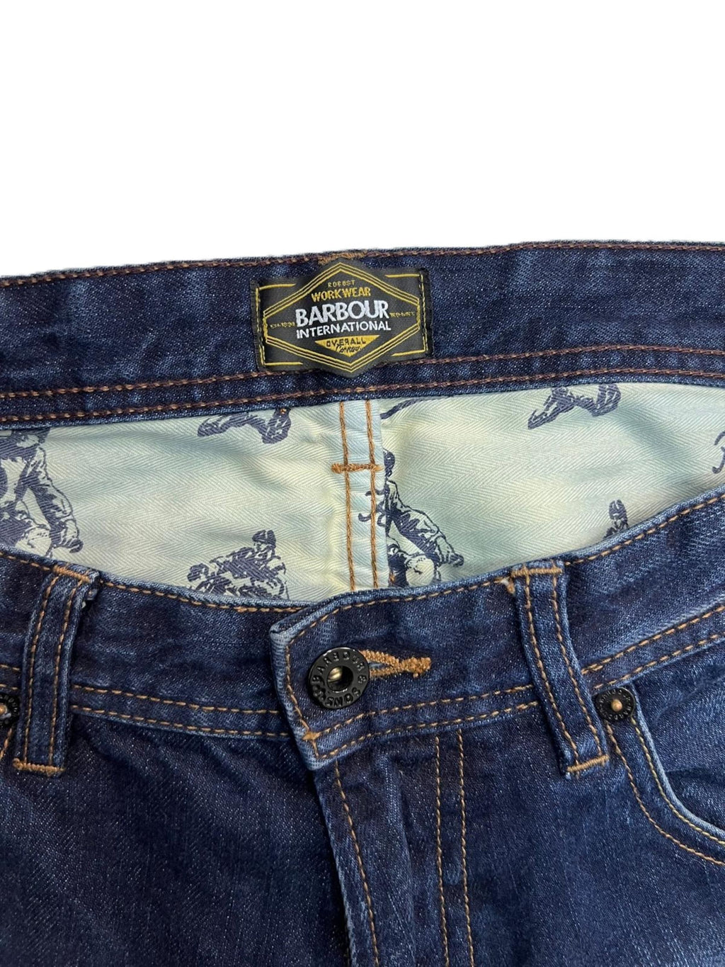 Primo piano della chiusura in vita dei jeans Barbour con focus sulla fodera interna stampata delle tasche frontali.