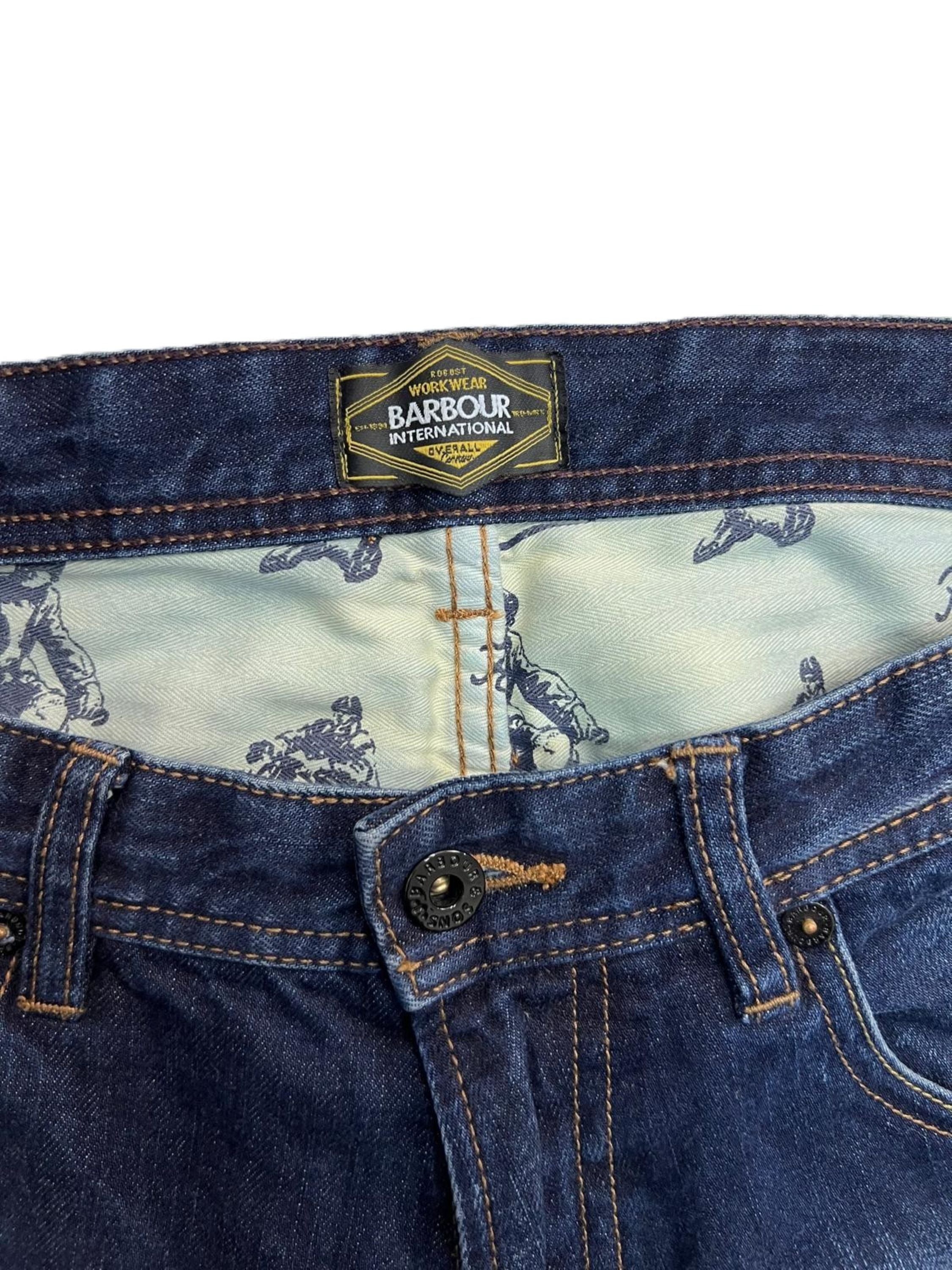  Primo piano della chiusura in vita dei jeans Barbour con focus sulla fodera interna stampata delle tasche frontali.