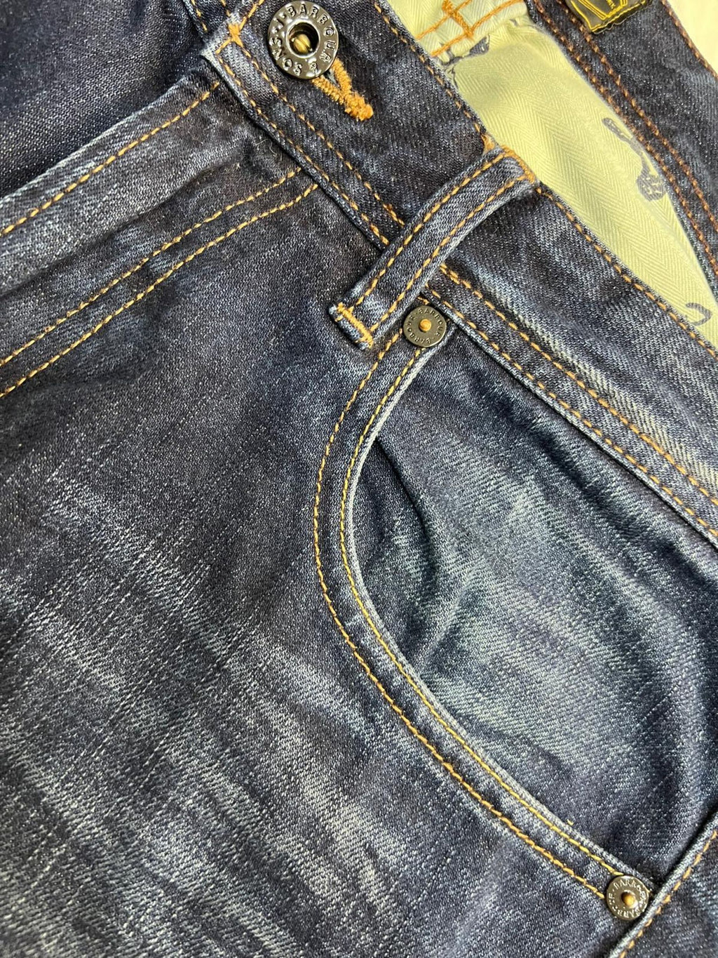 Dettaglio della tasca anteriore destra dei jeans Barbour con il taschino portamonete, le cuciture ocra e i rivetti metallici.