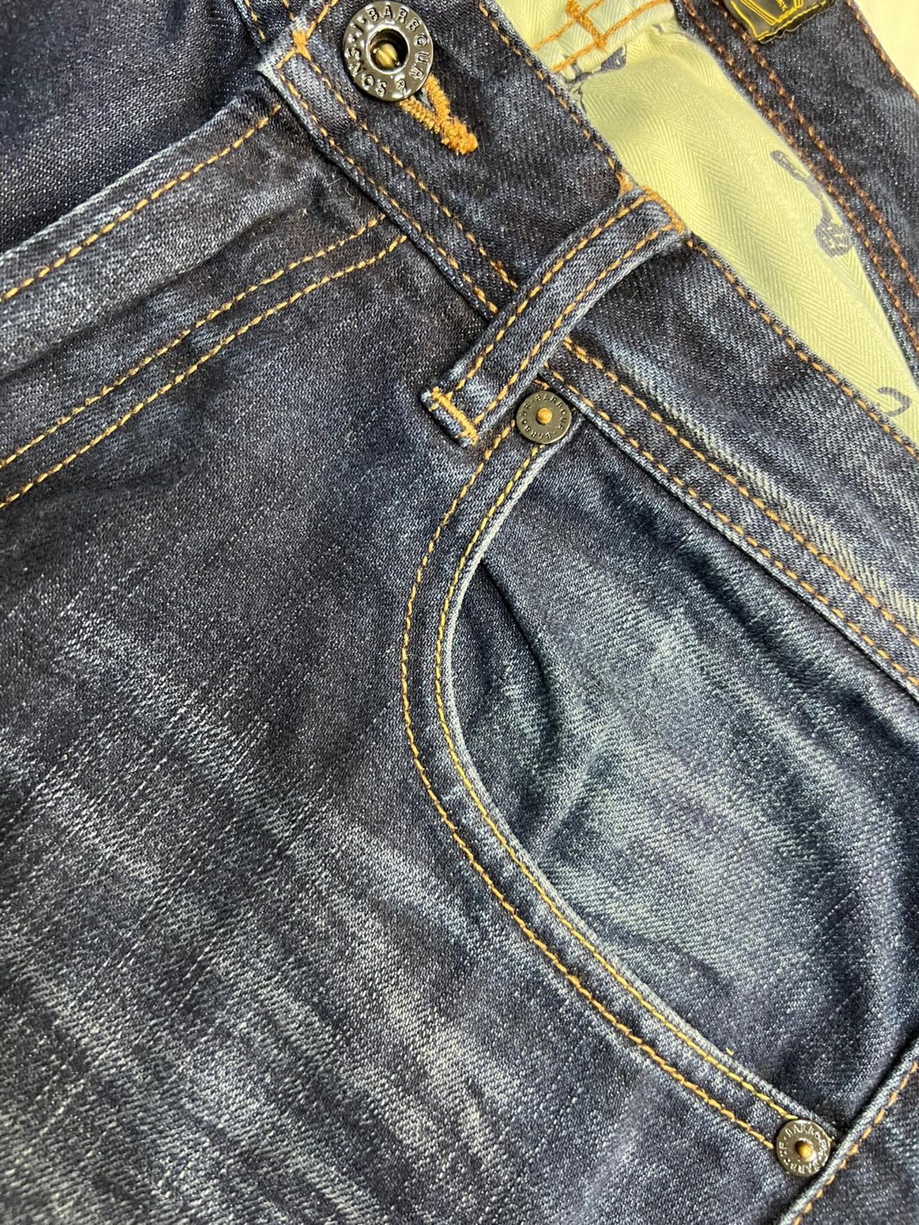 Dettaglio della tasca anteriore destra dei jeans Barbour con il taschino portamonete, le cuciture ocra e i rivetti metallici.