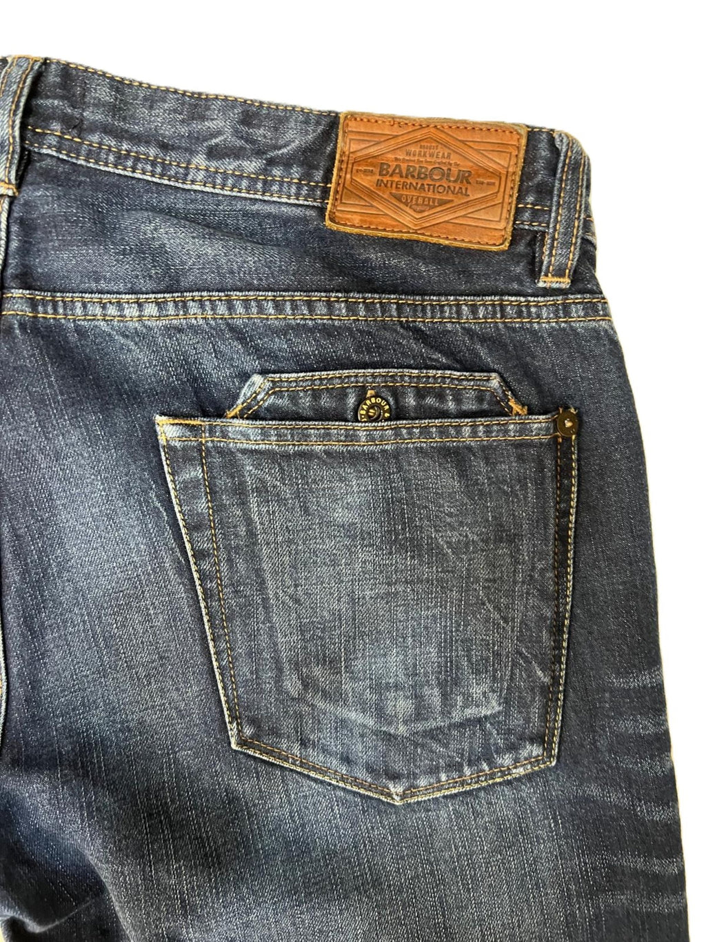 Inquadratura della tasca posteriore dei jeans Barbour con focus sulla salpa in pelle e sulla linguetta logata in tessuto.