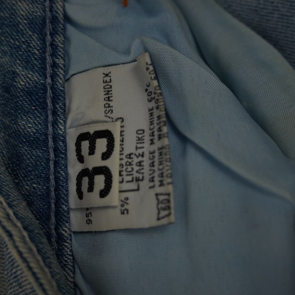 Etichetta interna in tessuto bianco che indica la taglia americana 33 e la composizione stretch con il 5% di licra spandex.