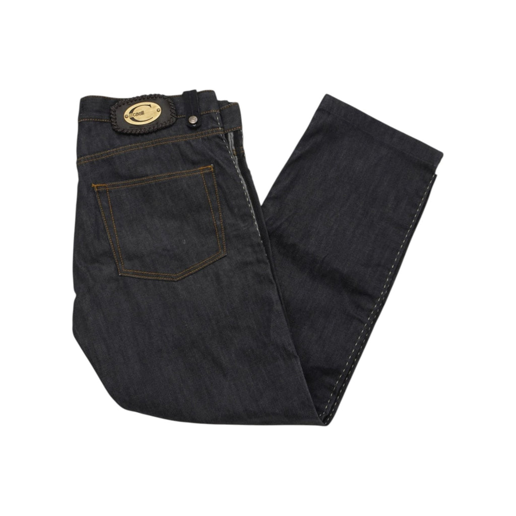 Jeans d'archivio Just Cavalli in denim rigido indigo scuro distesi di tre quarti, che mostrano la toppa con logo metallico dorato sul retro e il taglio dritto della gamba.