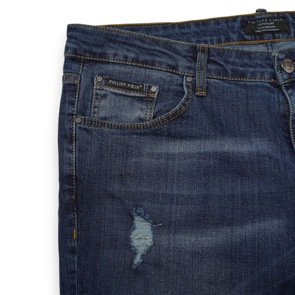 Dettaglio anteriore destro dei jeans uomo Philipp Plein con targa metallica sul taschino e strappo