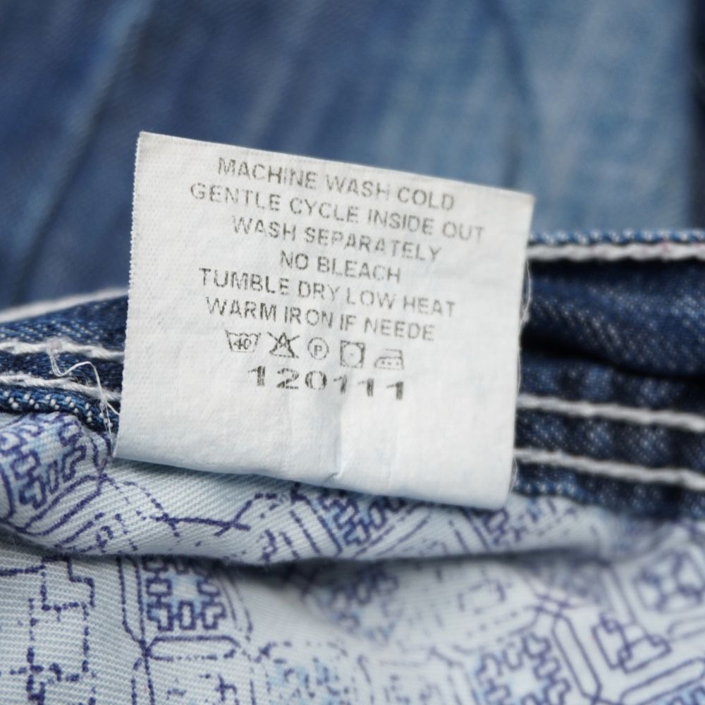 Dettaglio dell'etichetta interna con le istruzioni per il lavaggio in lavatrice a freddo e il codice numerico 120111 sui jeans True Religion.