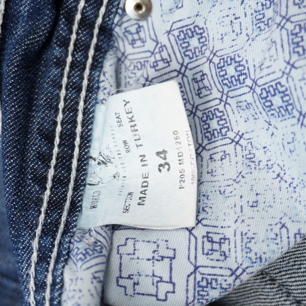 Dettaglio dell'etichetta interna stampata dei jeans True Religion che mostra la taglia 34, la produzione Made in Turkey, la composizione 100% cotone e la fodera della tasca logata.