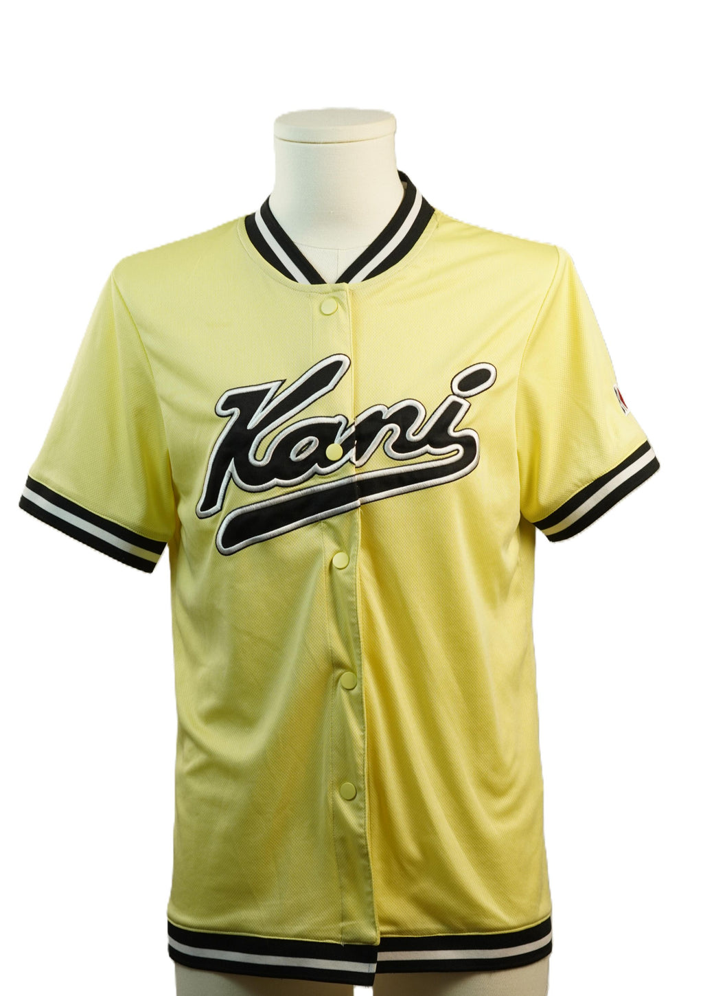 Vista frontale della maglia da baseball gialla abbottonata sul manichino, che evidenzia il logo Kani corsivo ricamato in nero e argento sul petto.
