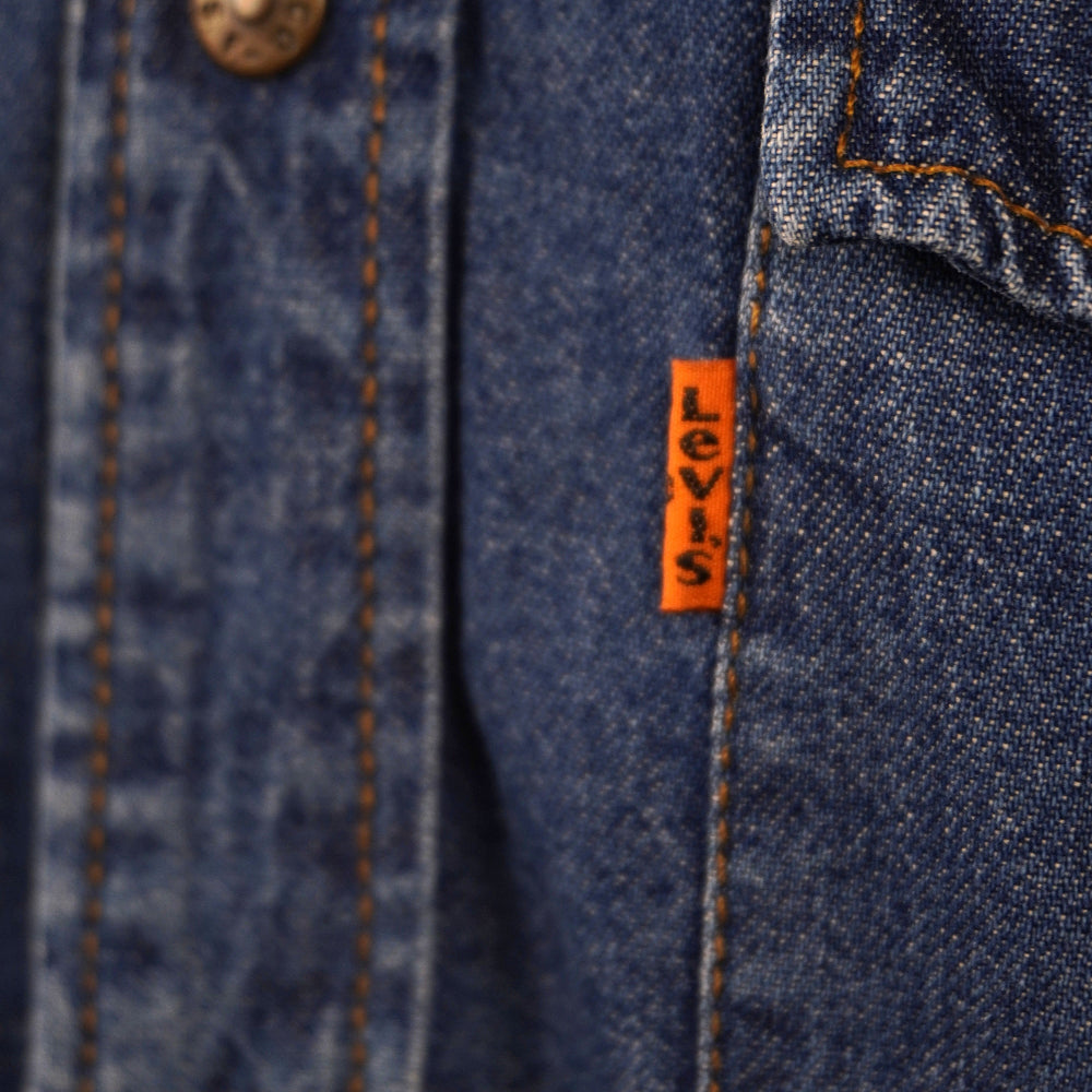 Dettaglio macro dell'iconica linguetta arancione Orange Tab con il marchio Levi's cucita verticalmente sul bordo della tasca frontale.