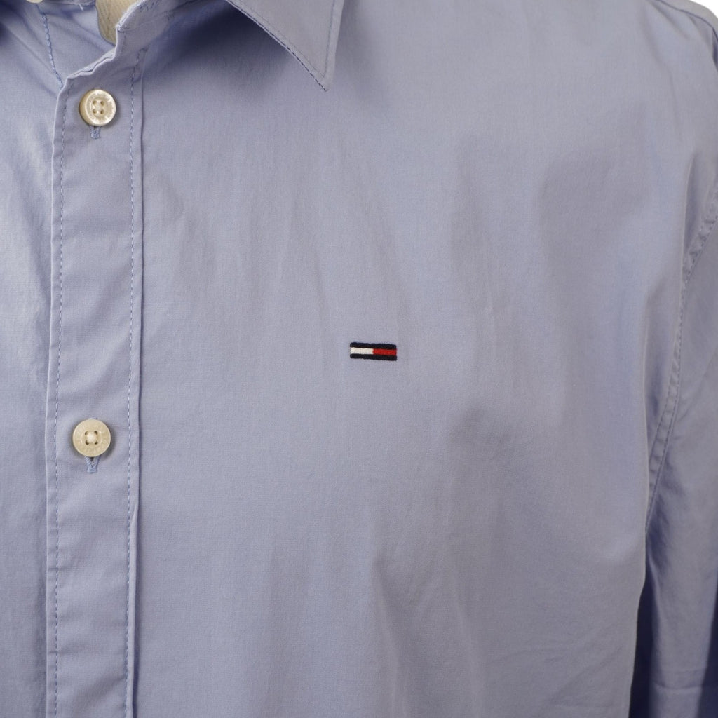 Primo piano del logo flag di Tommy Jeans ricamato sul petto del tessuto celeste.