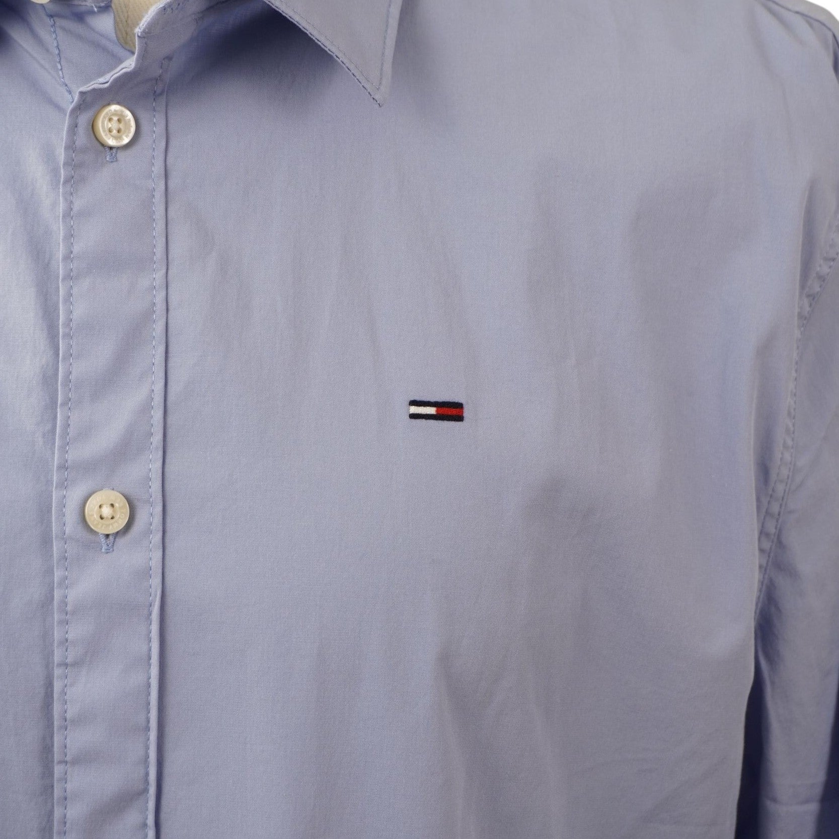 Primo piano del logo flag di Tommy Jeans ricamato sul petto del tessuto celeste.