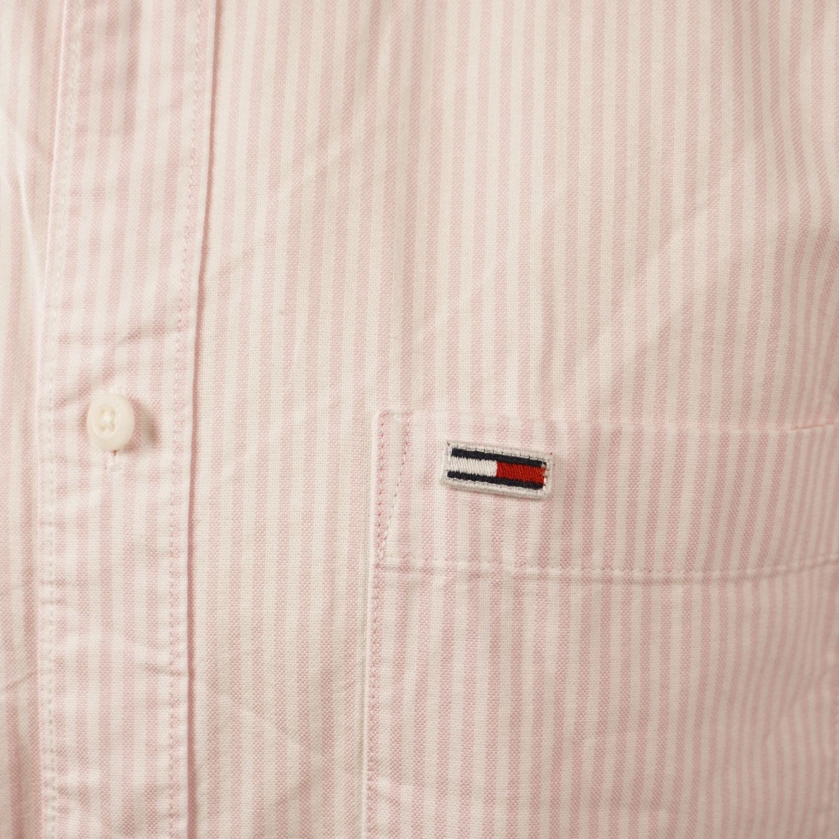 Primo piano del celebre logo flag di Tommy Jeans ricamato sul petto del tessuto Oxford rosa.