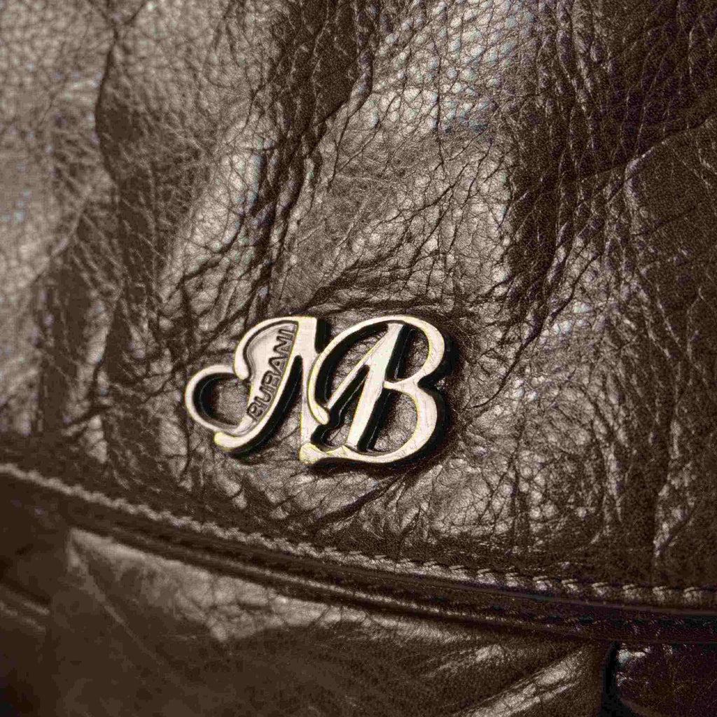 Primo piano del logo metallico dorato con le iniziali MB intrecciate sulla patta in pelle marrone.