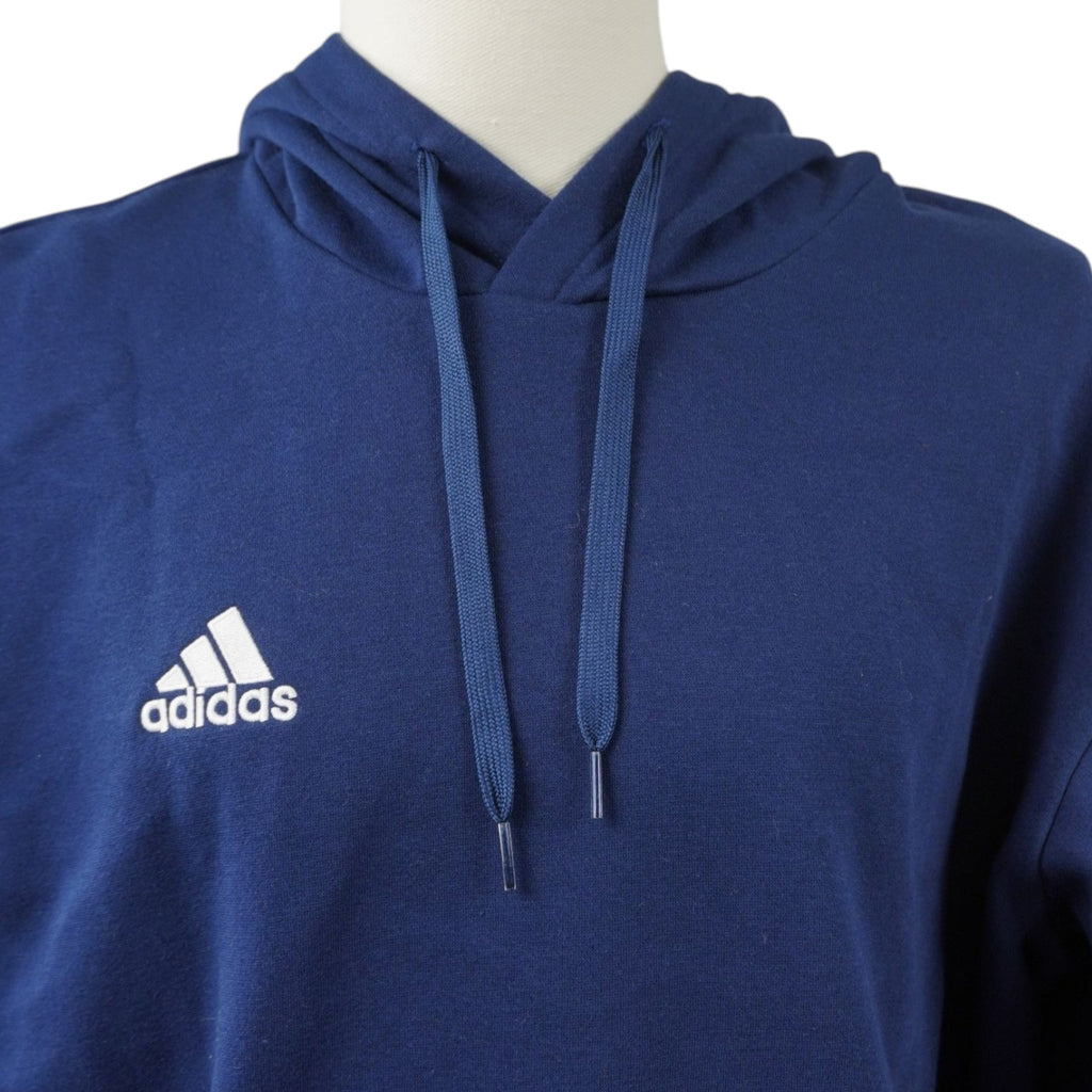 Dettaglio ravvicinato del logo bianco "Badge of Sport" di adidas ricamato a contrasto sul tessuto blu scuro della felpa.
