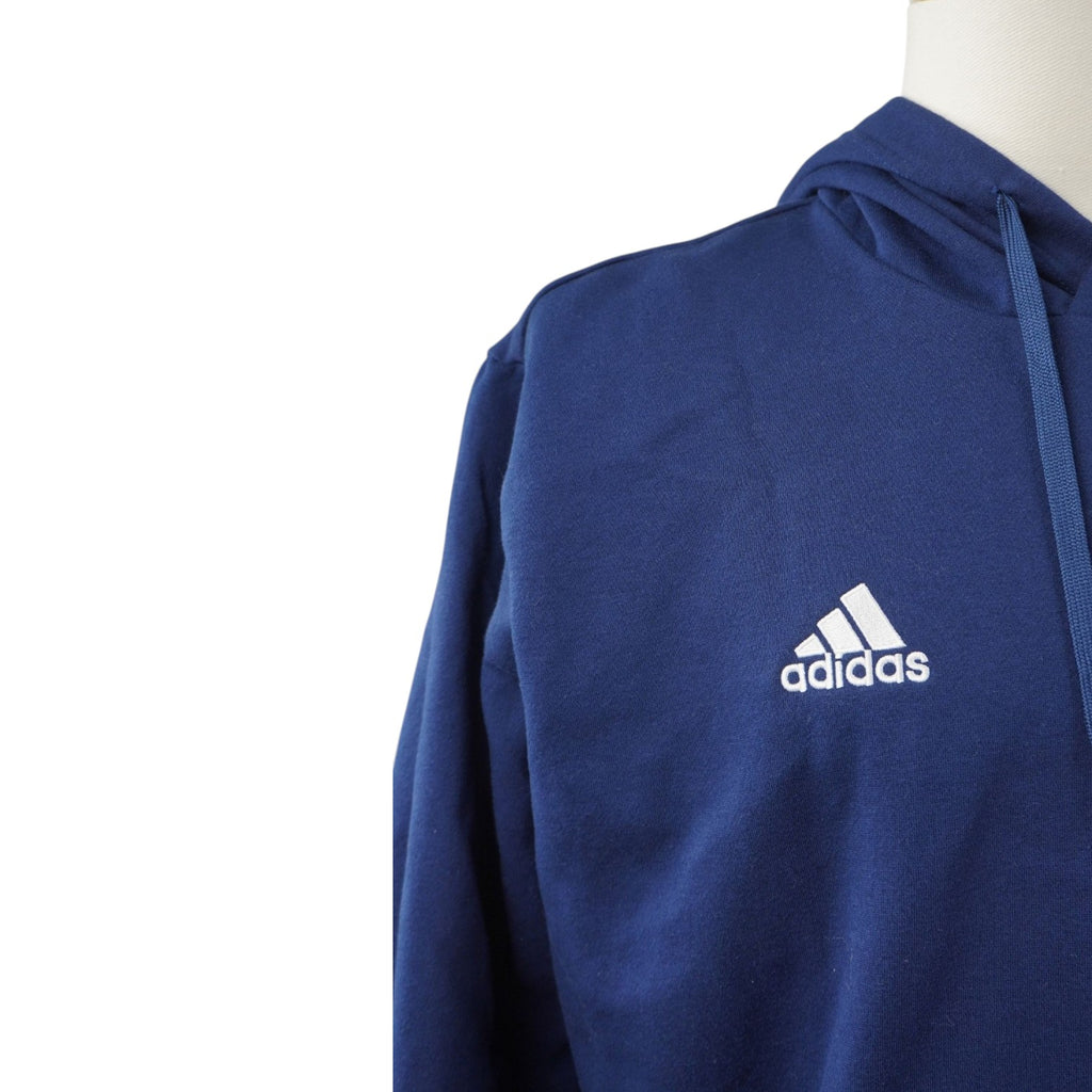Dettaglio ravvicinato del logo bianco "Badge of Sport" di adidas ricamato a contrasto sul tessuto blu scuro della felpa.