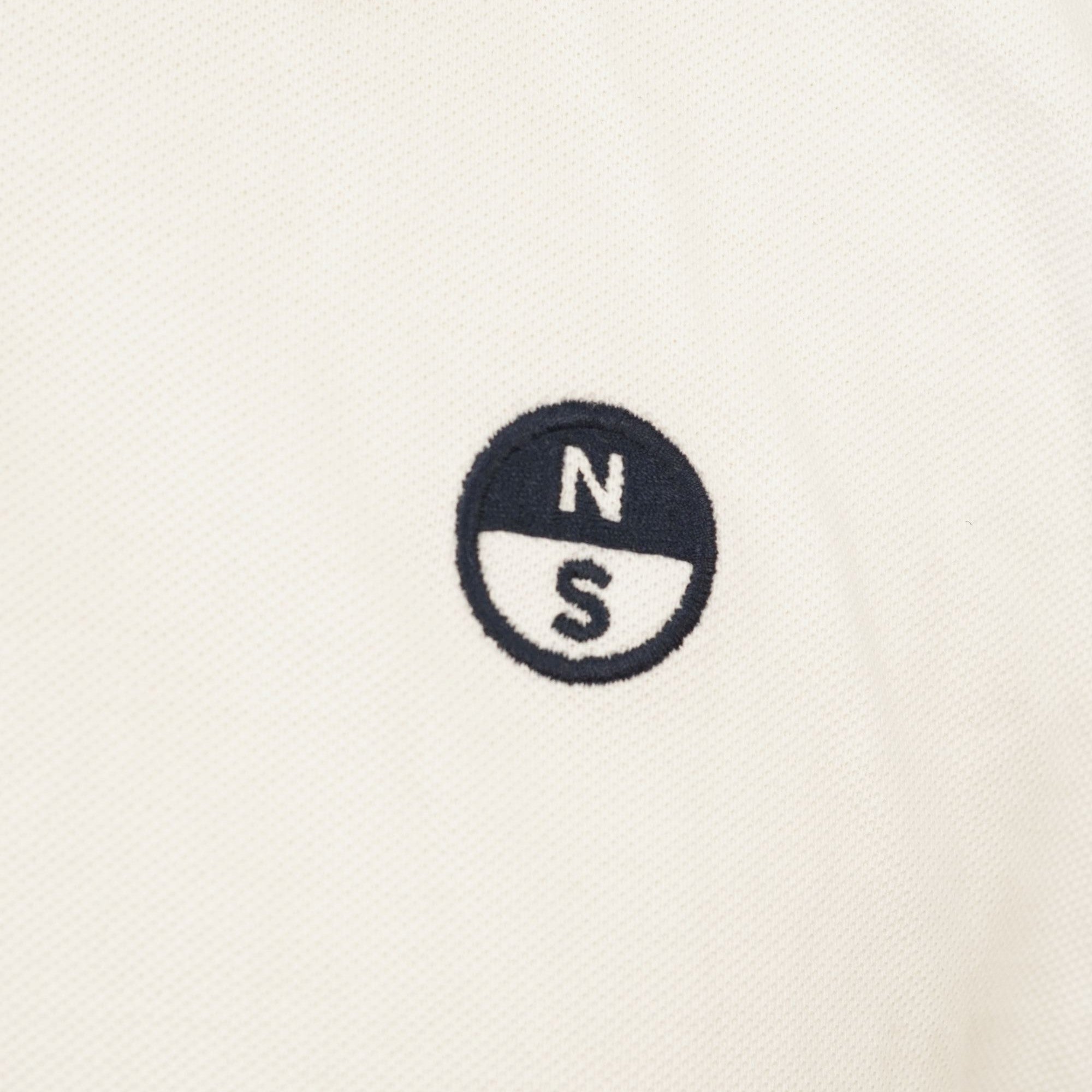 Primo piano del logo tondo ricamato North Sails applicato sul petto, diviso orizzontalmente in bianco e blu navy con lettere N e S.
