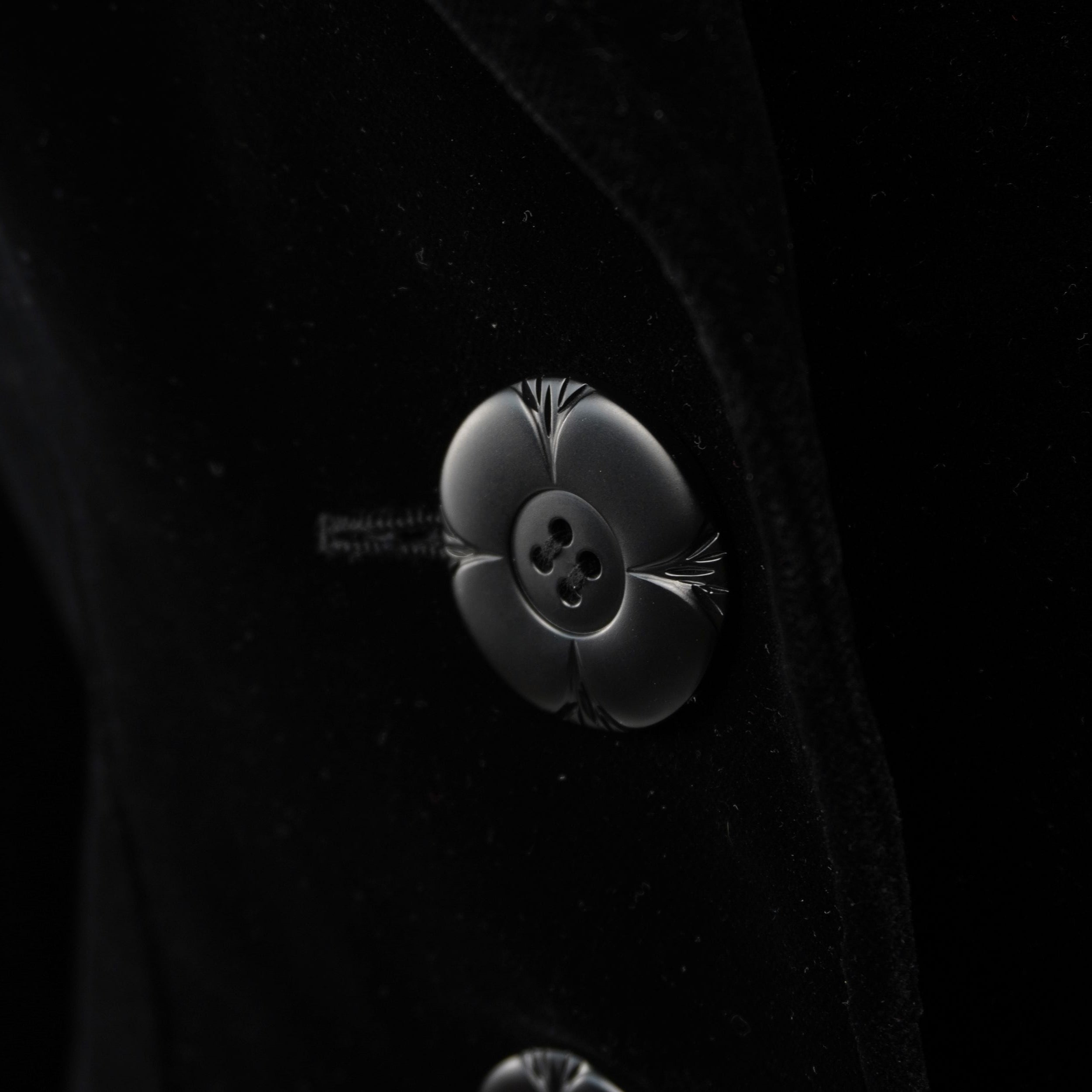 Macro di un singolo bottone floreale a rilievo, dettaglio dell'artigianalità del brand Petite Mademoiselle.